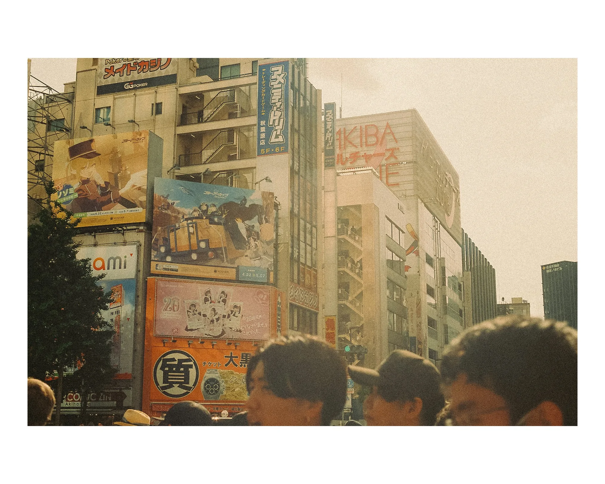City street scene with tall buildings covered in colorful advertisements and signs, and a crowd of people in the foreground walking and standing.