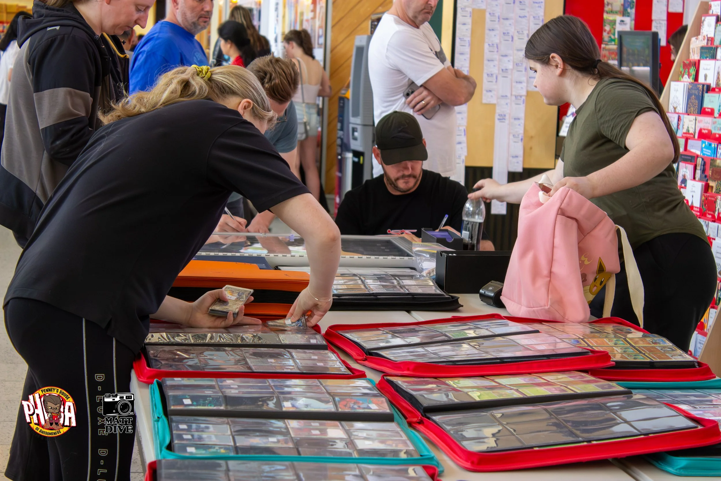 People browsing and inspecting trading cards at a table in a store, with multiple binders filled with cards on display.