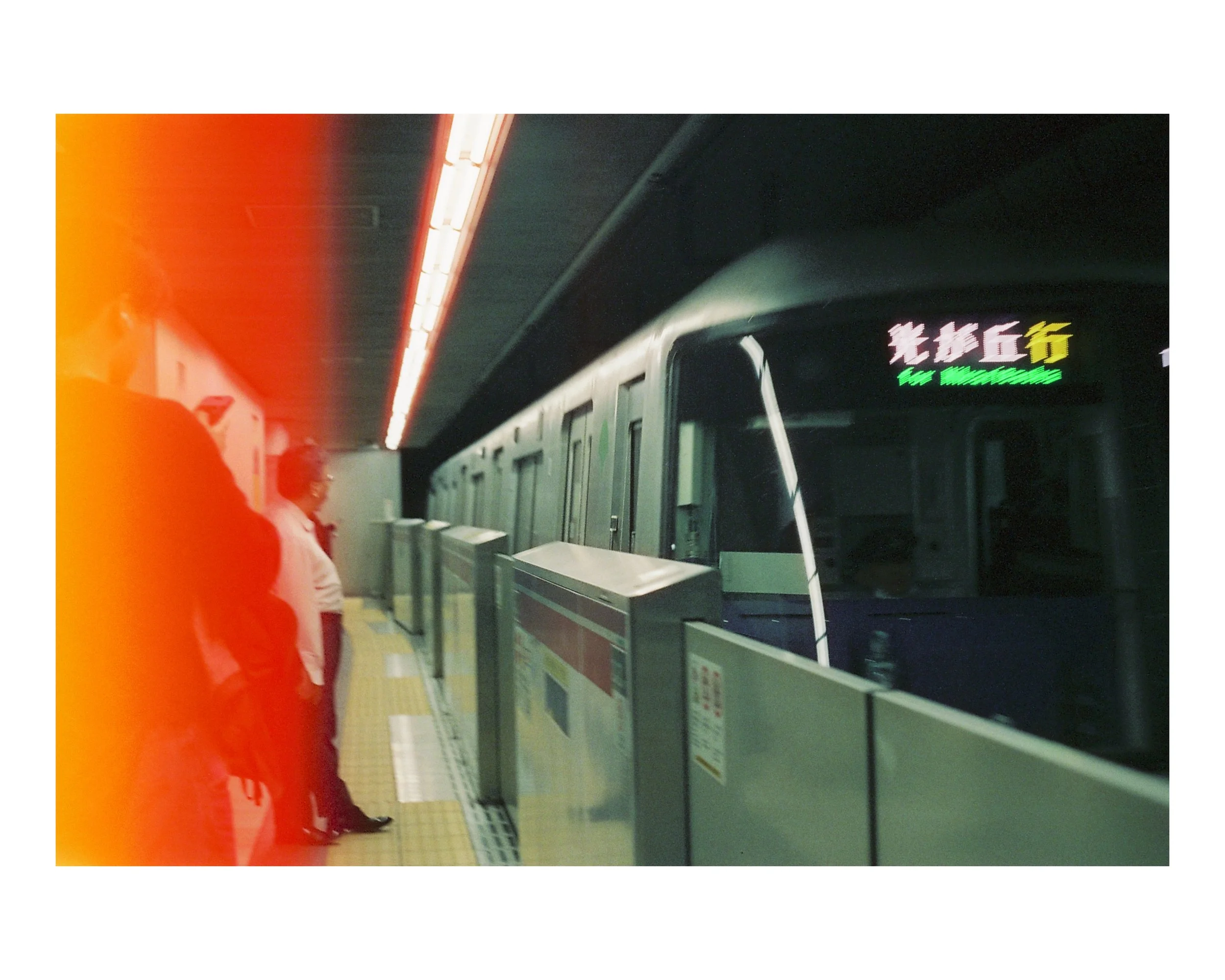Subway station platform with train and several passengers waiting, illuminated sign on train displays destination in Chinese and English