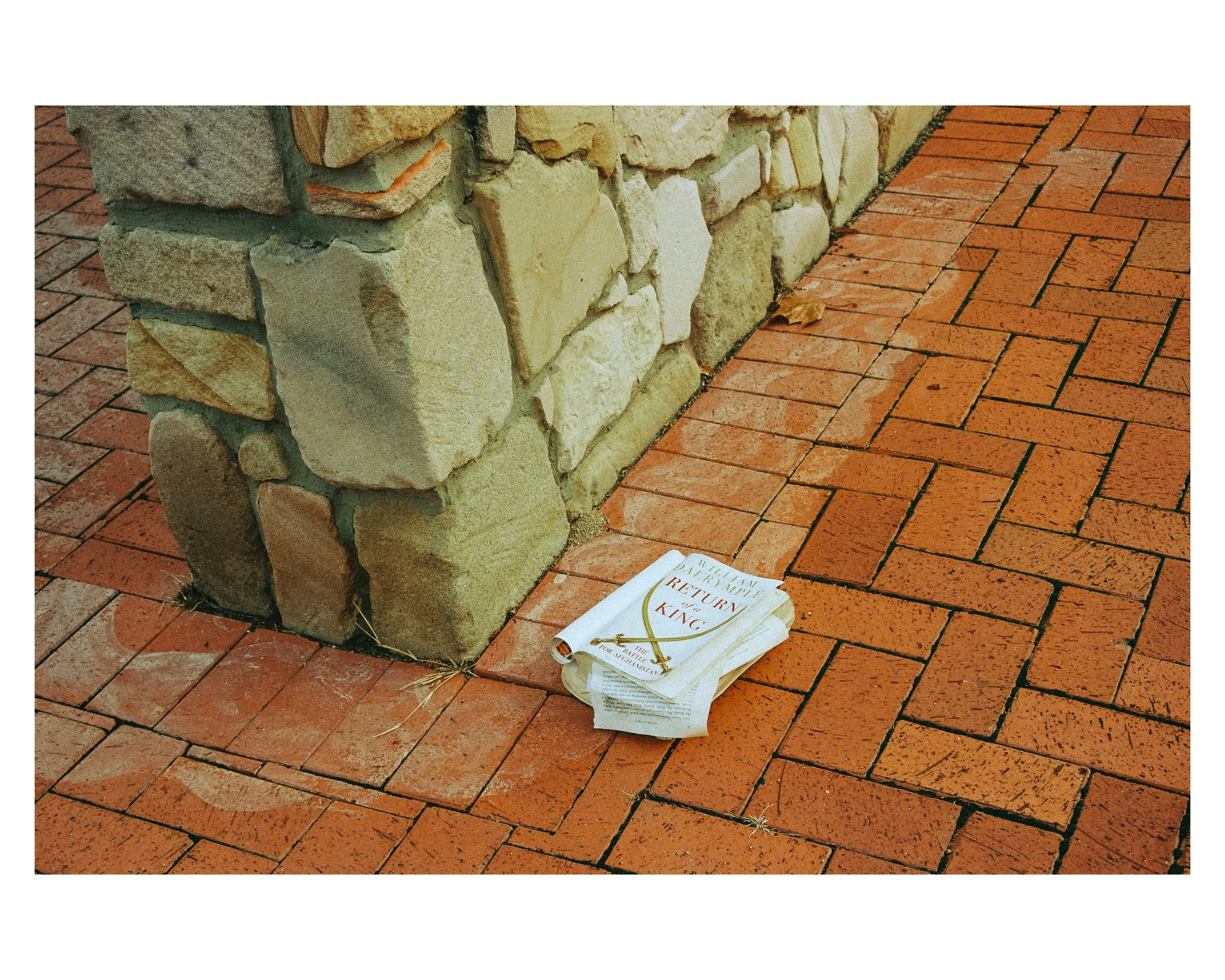 A crumpled paperback book titled 'Return of the King' lying on a brick sidewalk near a stone wall.