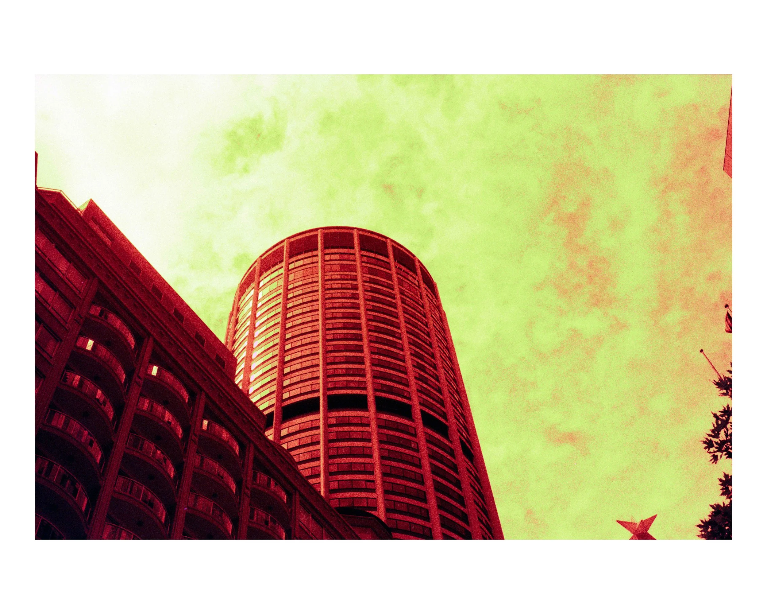 Low-angle view of tall modern building with curved facade against a colorful sky with green and yellow hues.