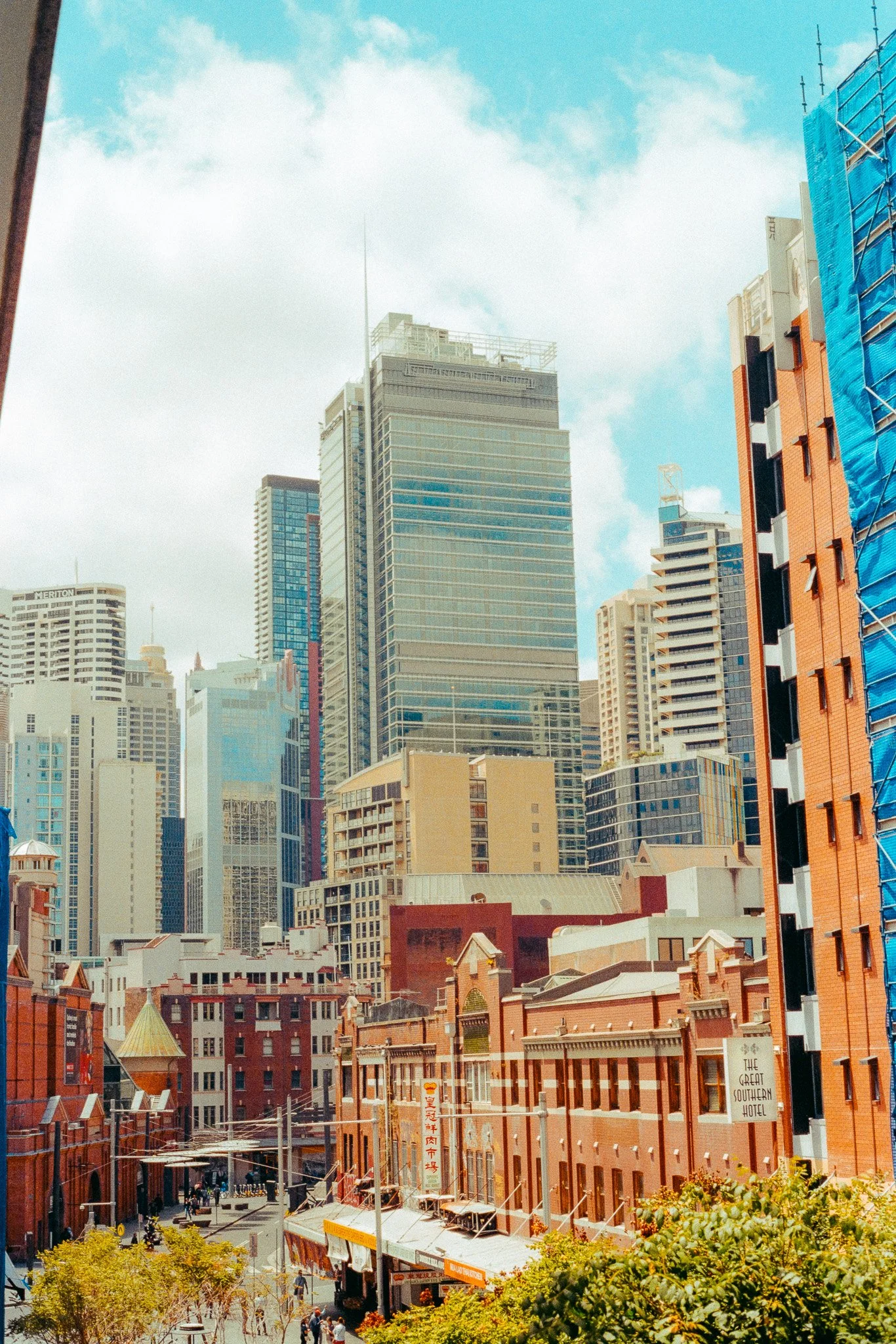 Cityscape with modern skyscrapers and historic red brick buildings, blue sky, and clouds.