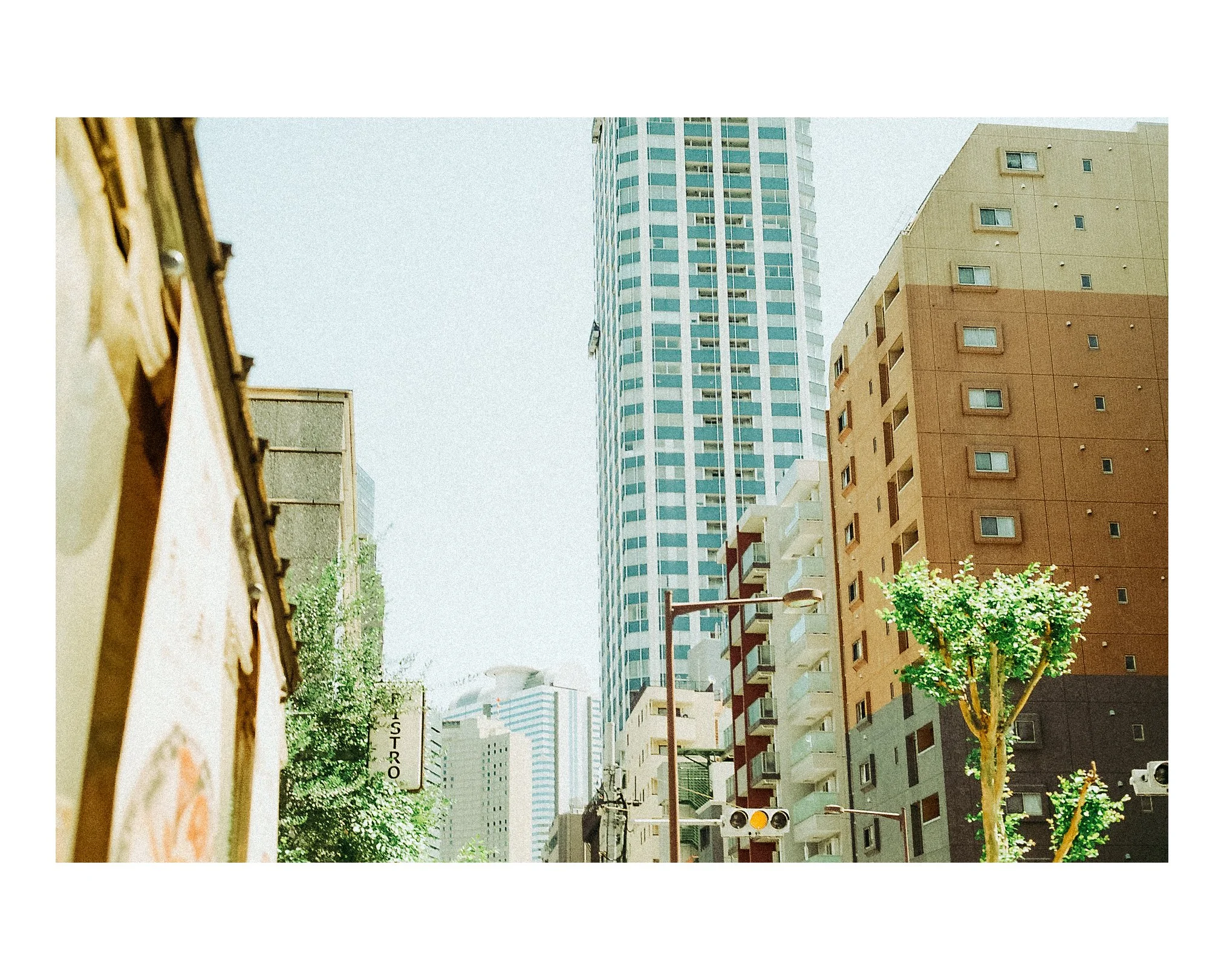 Cityscape with tall modern buildings, trees, and streetlights under a clear sky.