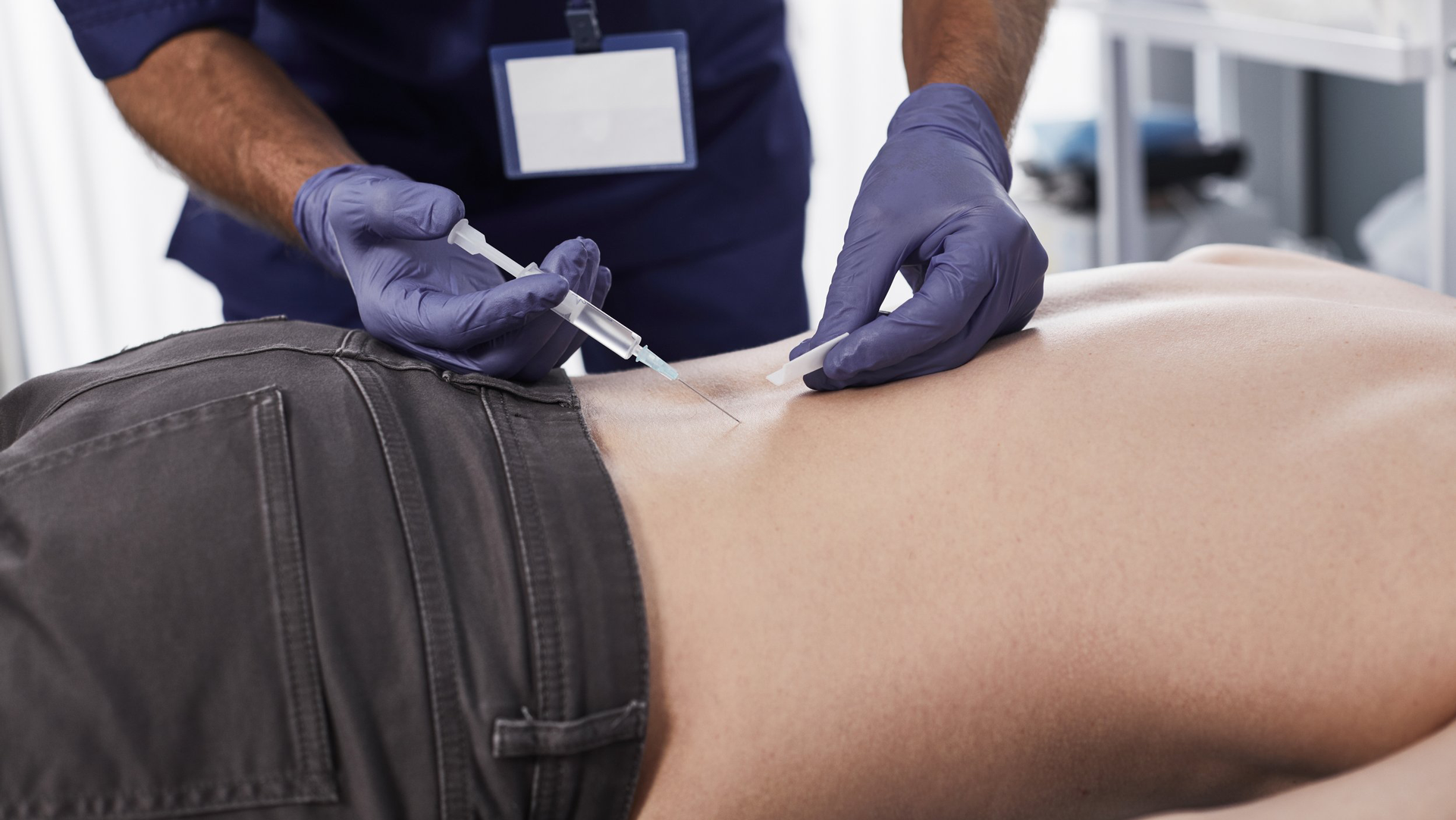 A healthcare professional is administering a prolozone injection into a patient's back while wearing purple gloves.