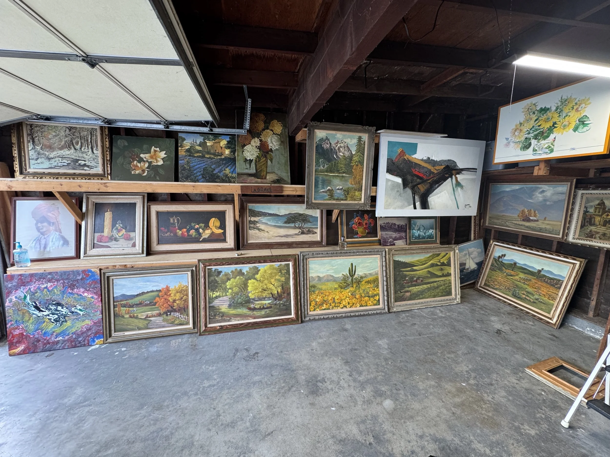 Gallery of landscape and nature paintings displayed on a wooden wall in an art studio or gallery space with a concrete floor.
