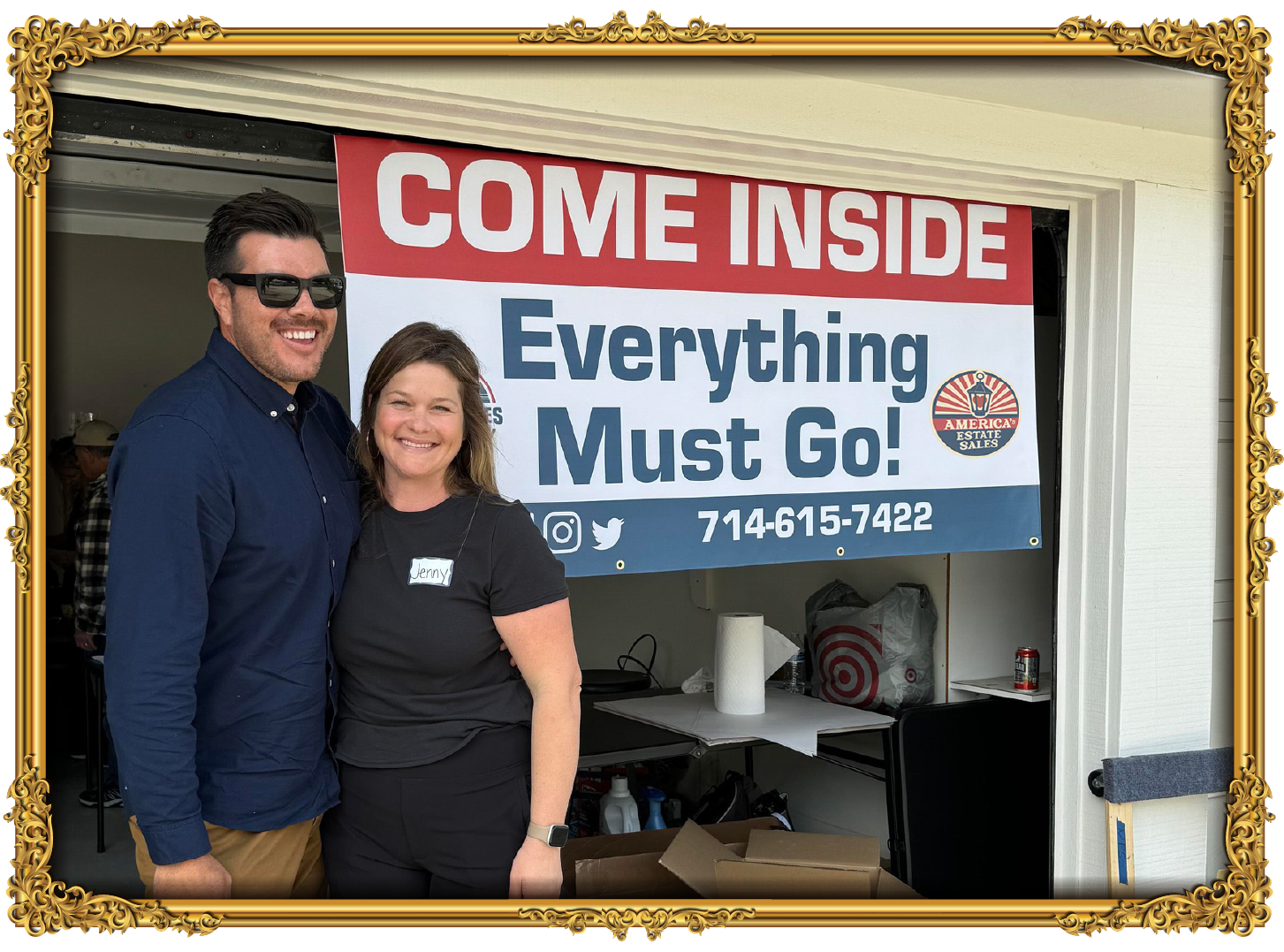 Two smiling people standing in front of a large sign that reads 'Come Inside Everything Must Go!' at an estate sale. The man is wearing a navy blue shirt and glasses, and the woman is wearing a black shirt with a name tag that says 'Jenny.'