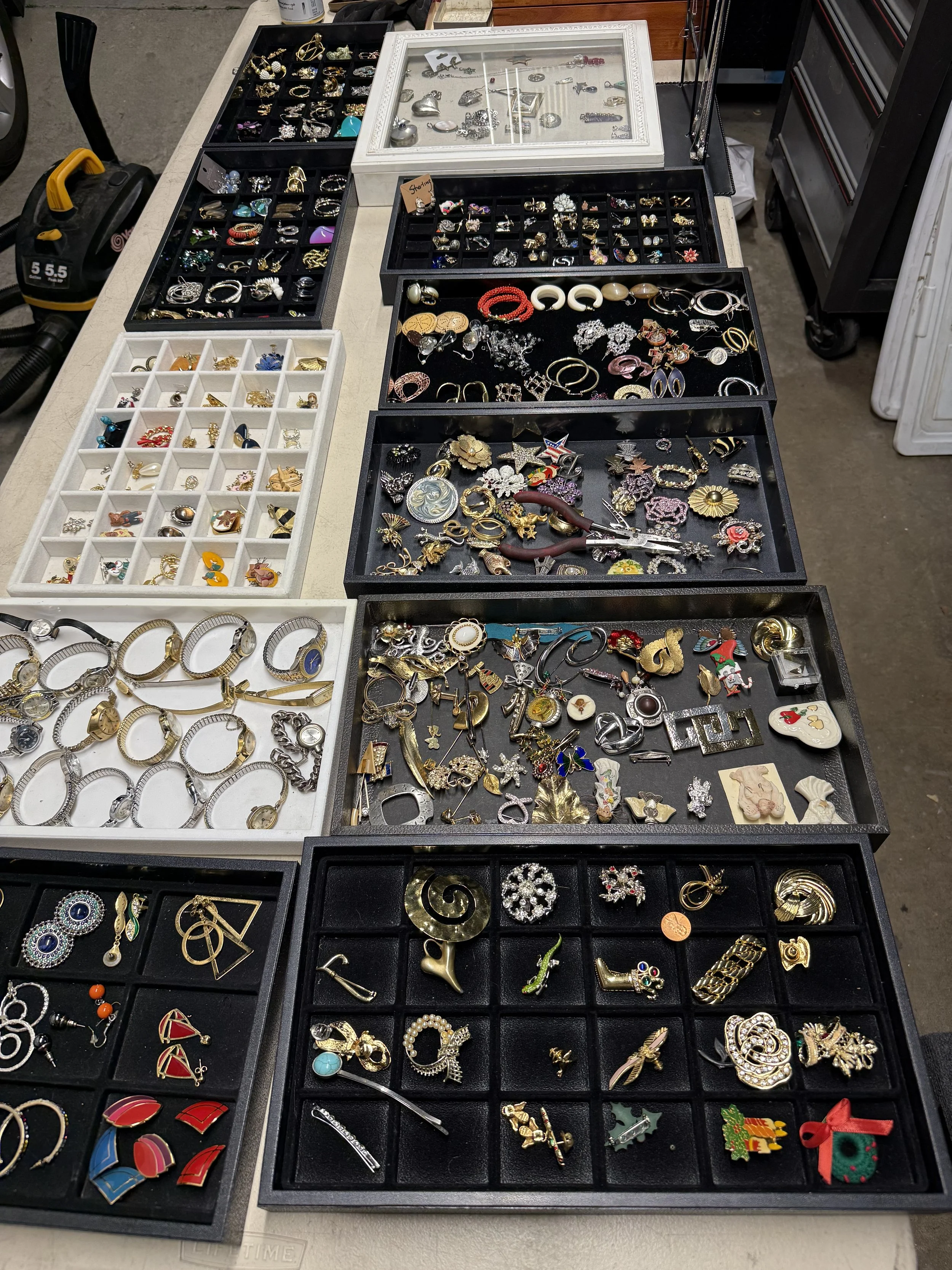 A table displaying an assortment of jewelry including earrings, rings, brooches, and necklaces in various trays and cases, some with decorative holiday themed pieces.