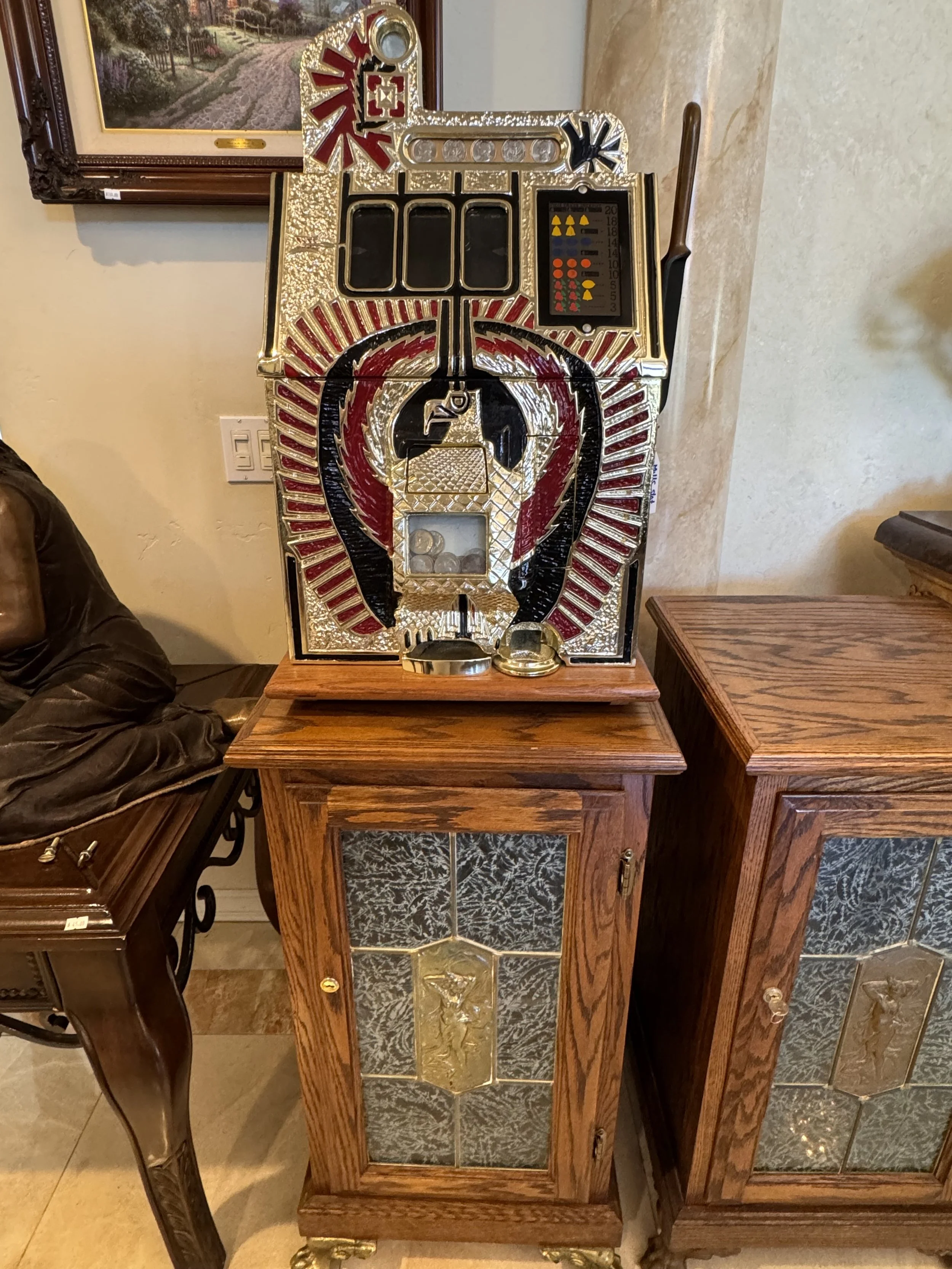 A vintage slot machine with decorative red, black, and gold accents, featuring a wooden cabinet with ornate carved details, displaying coins at the bottom, and a set of buttons and a display panel on top.