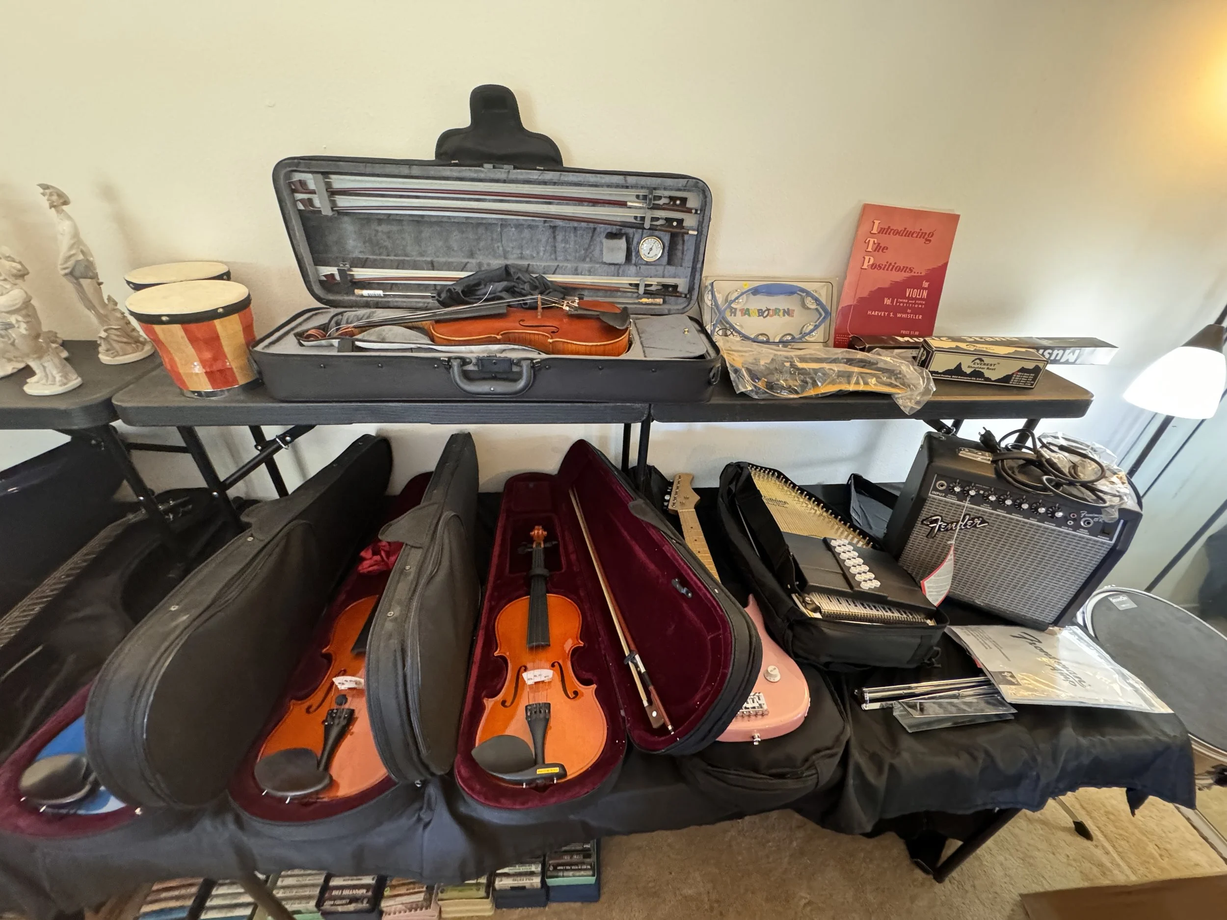 Table holding violin cases, a few figurines, a musical book, and music equipment including a small amplifier and a guitar.