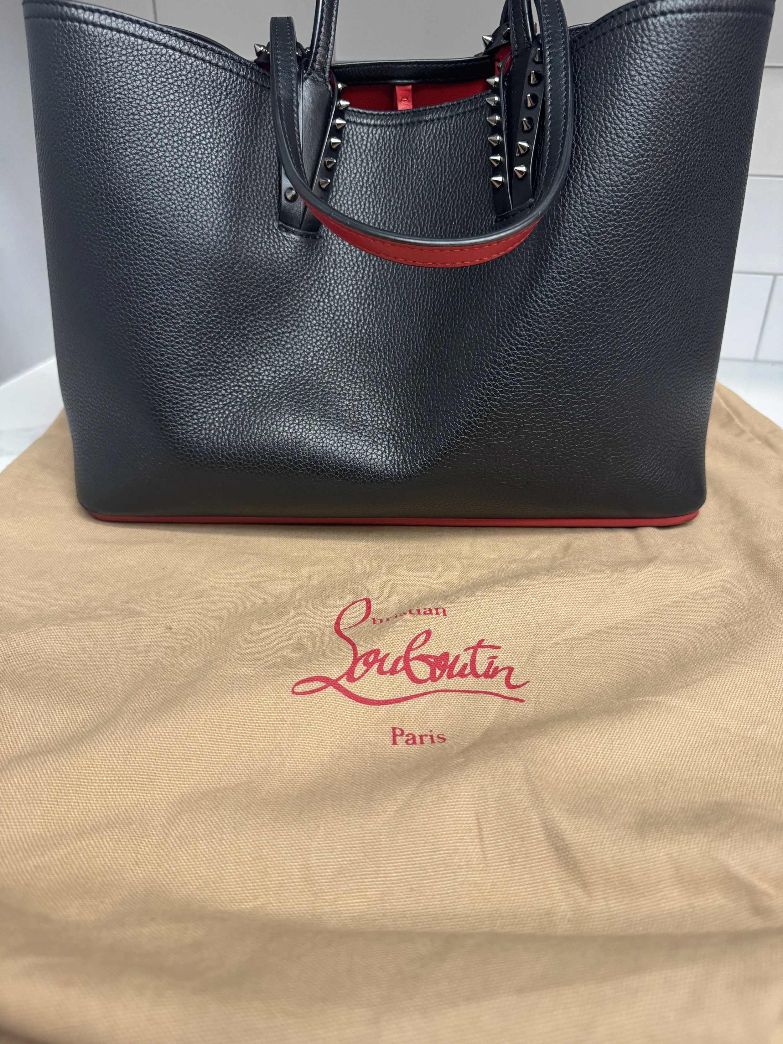 Black Louis Vuitton tote bag with red accents and studded handles, sitting on a beige Louis Vuitton dust bag with red lettering.