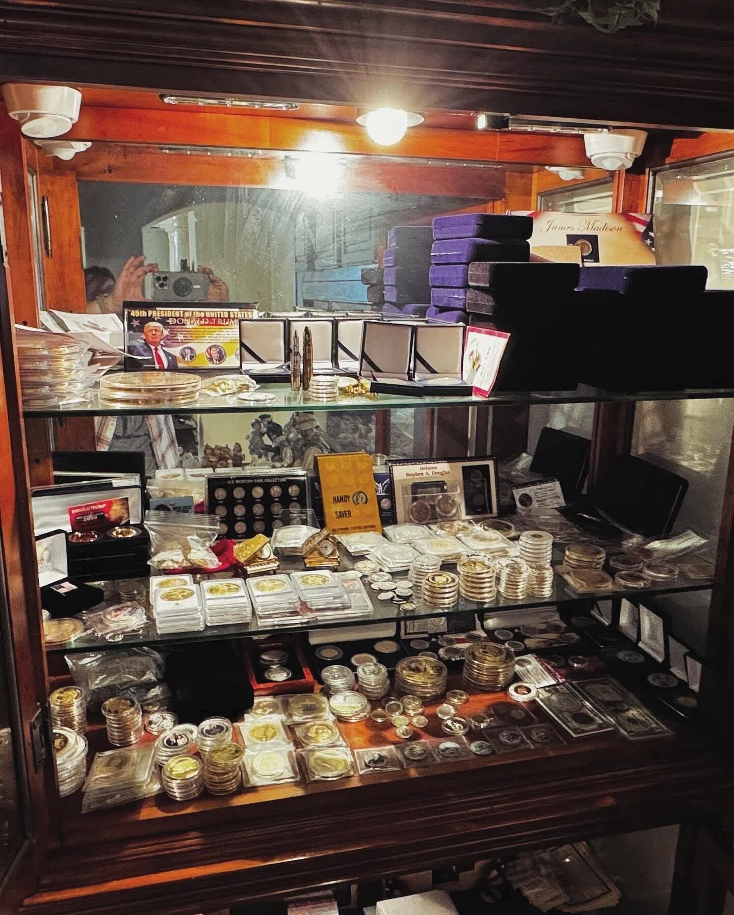 Display case filled with various collectible coins, medals, and tokens, with some stacks and organized rows, reflecting in the glass.