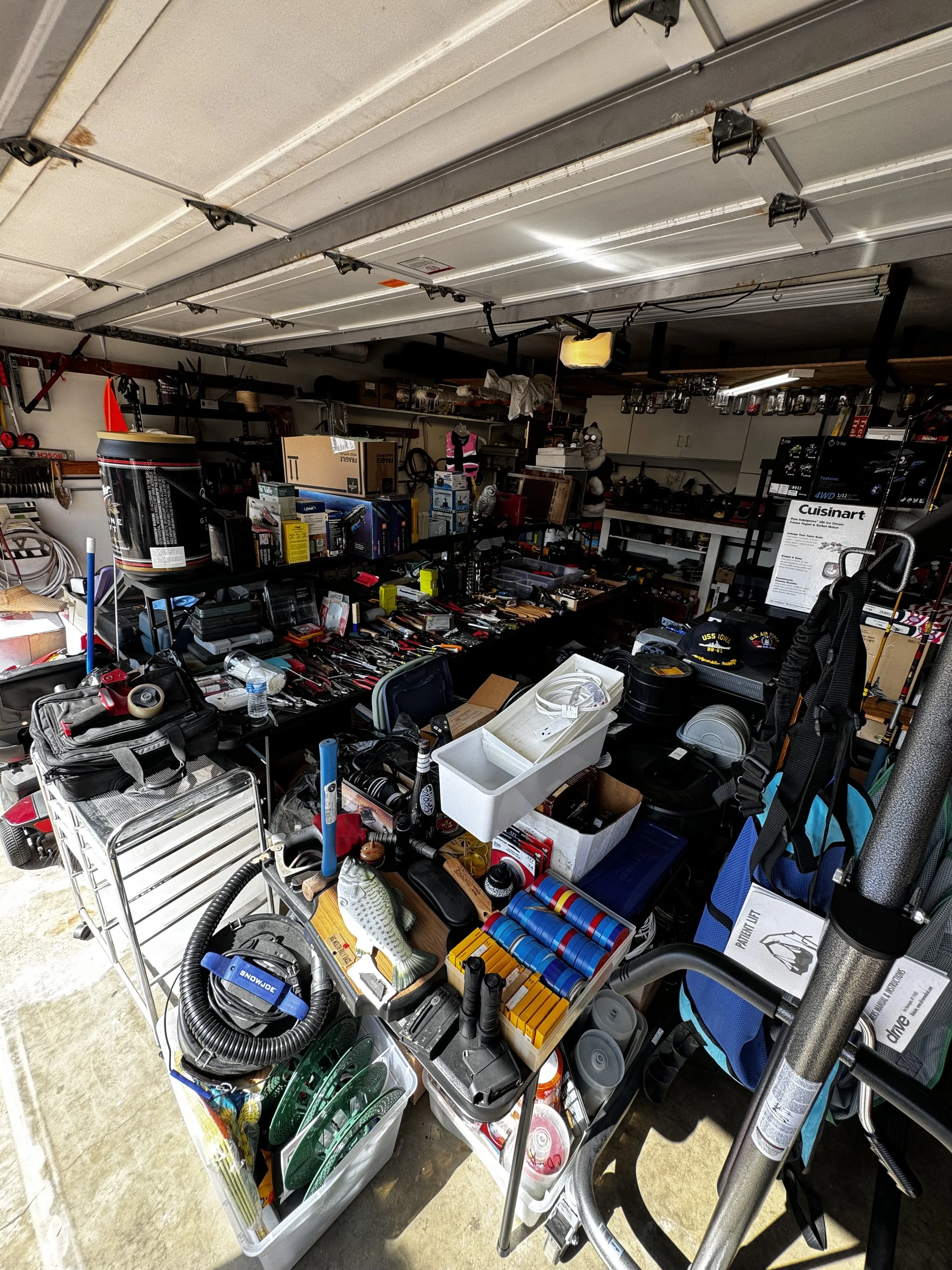 A cluttered garage organizing shelf filled with various tools, equipment, boxes, and miscellaneous household items.