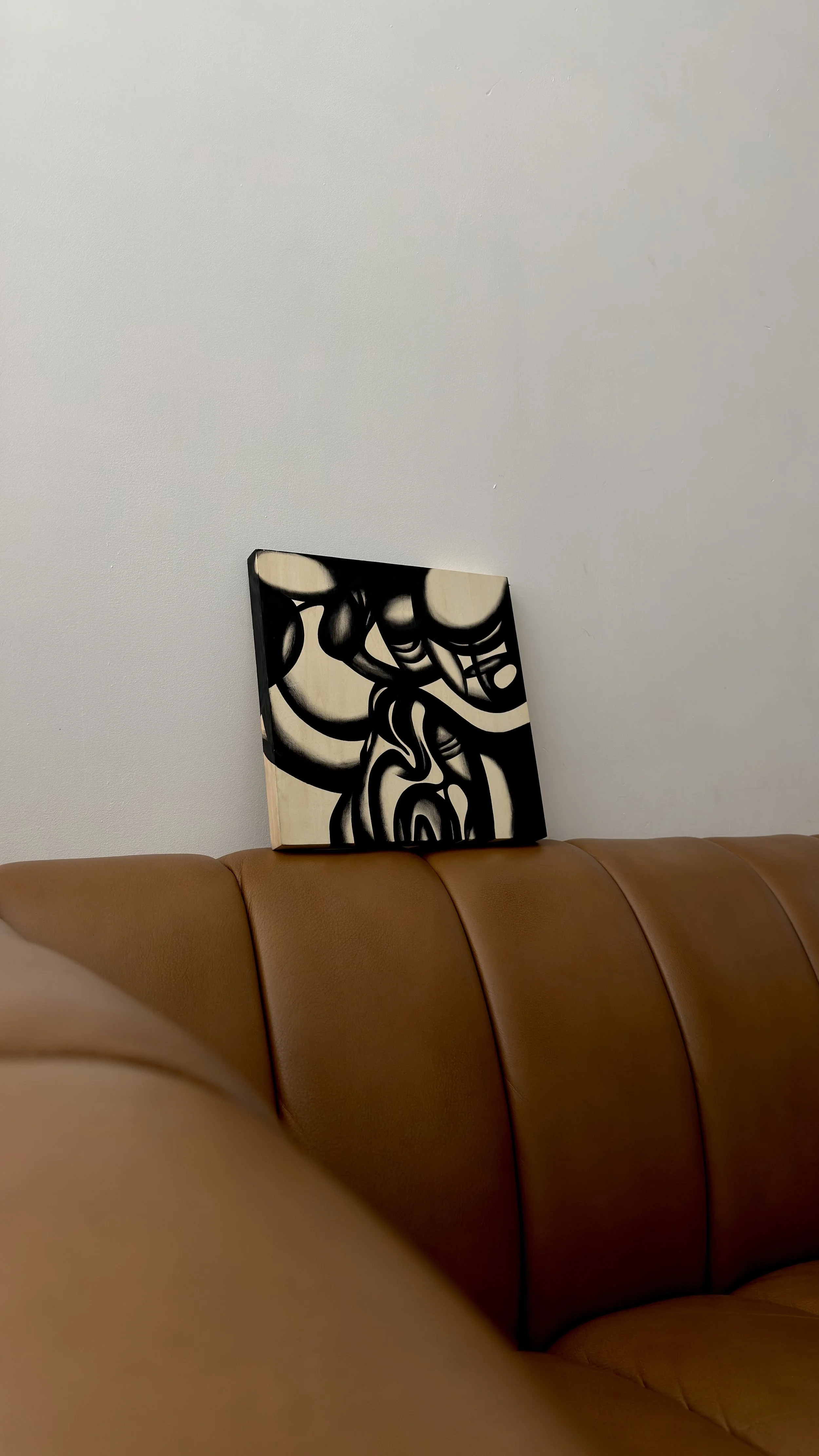 A modern abstract black and white painting resting against a plain white wall, placed behind a brown leather sofa.