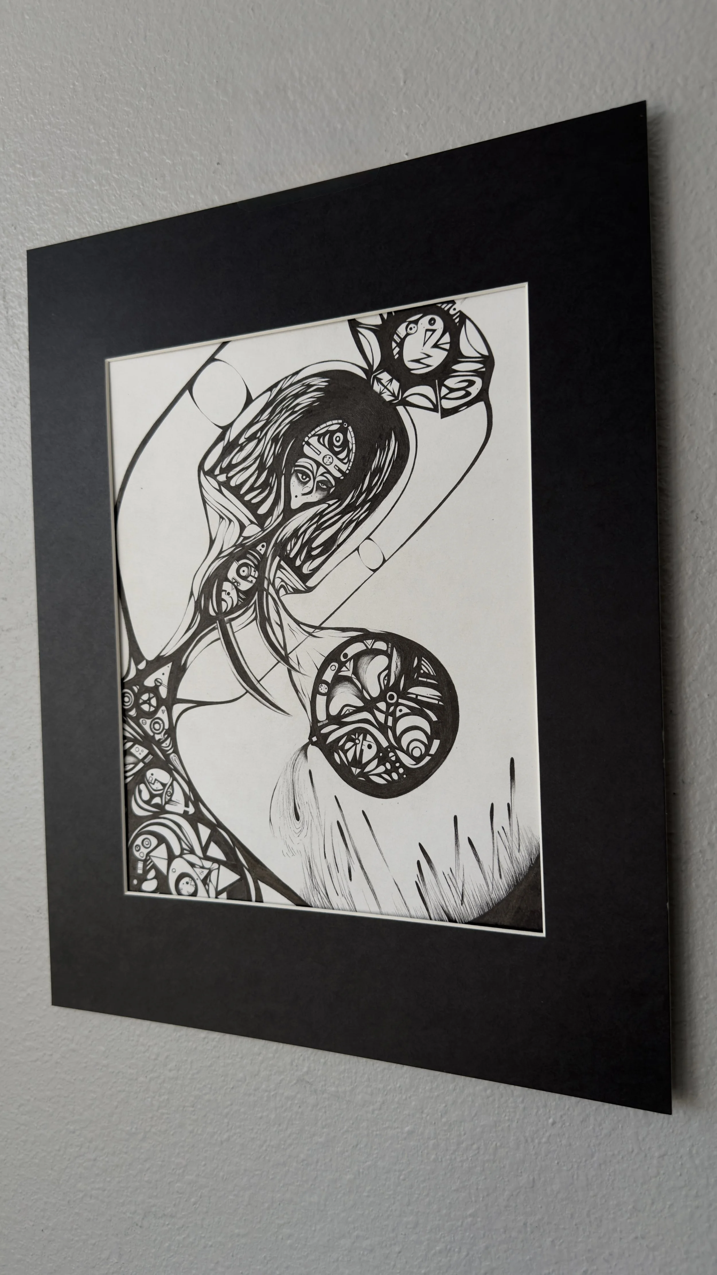 Black and white abstract art with interconnected shapes and patterns, including circles, triangles, and lines, framed in a black border on a white wall.