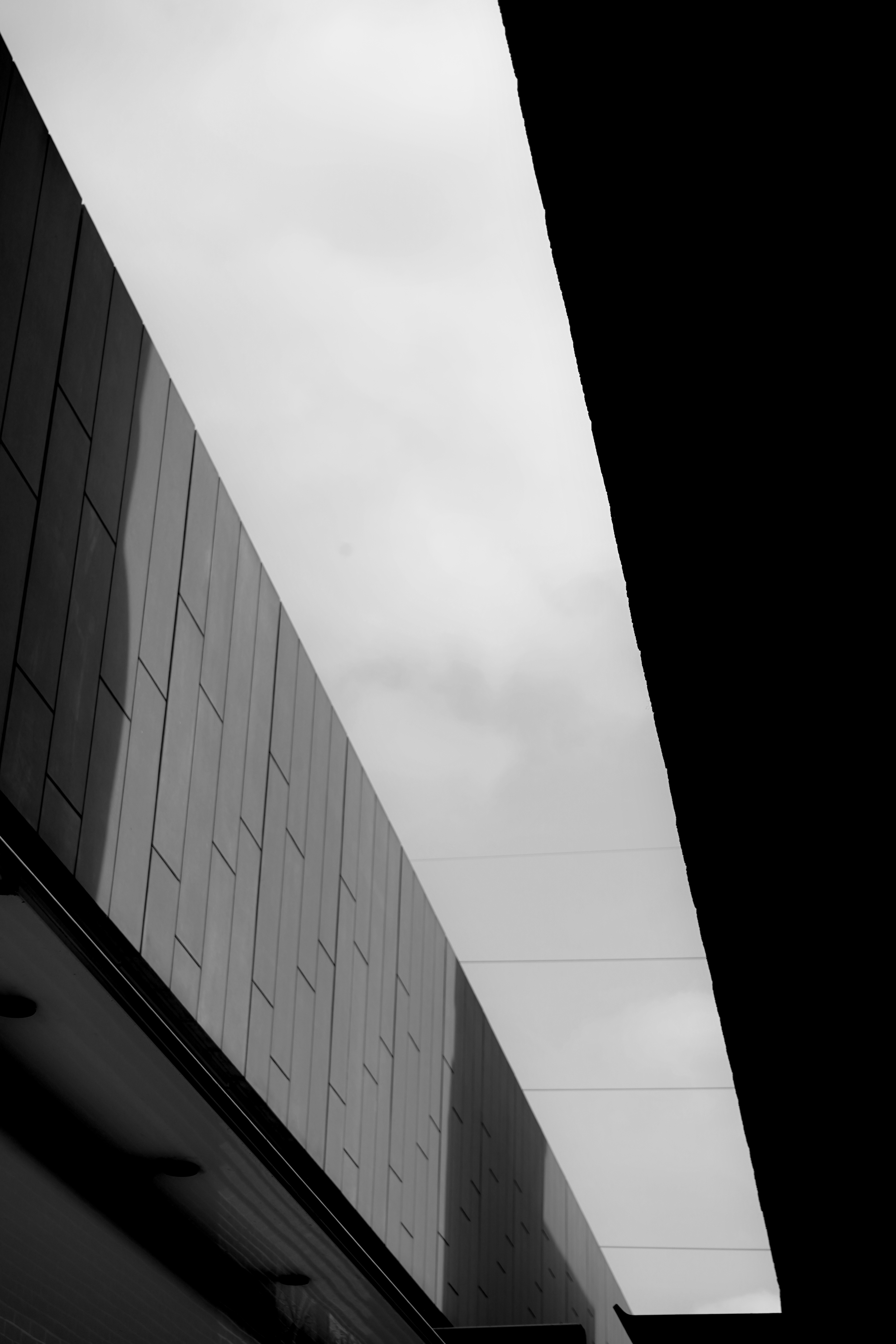 A photo showing the exterior corner of a modern building with sleek, reflective panels and an overhanging roof, taken during daytime under cloudy skies.