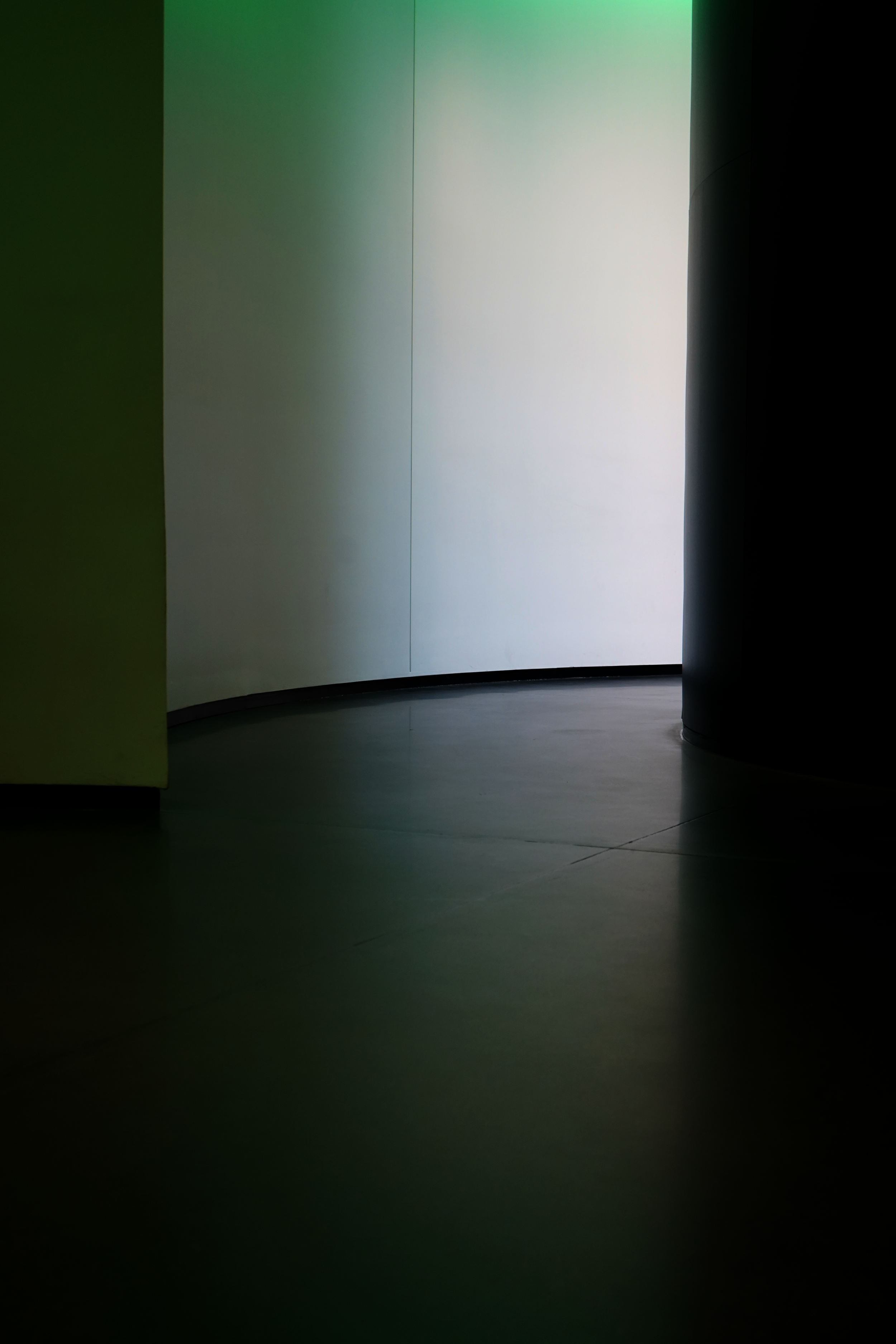 A dimly lit hallway in an art museum with a bright white wall at the end, and a curved door on the right side.