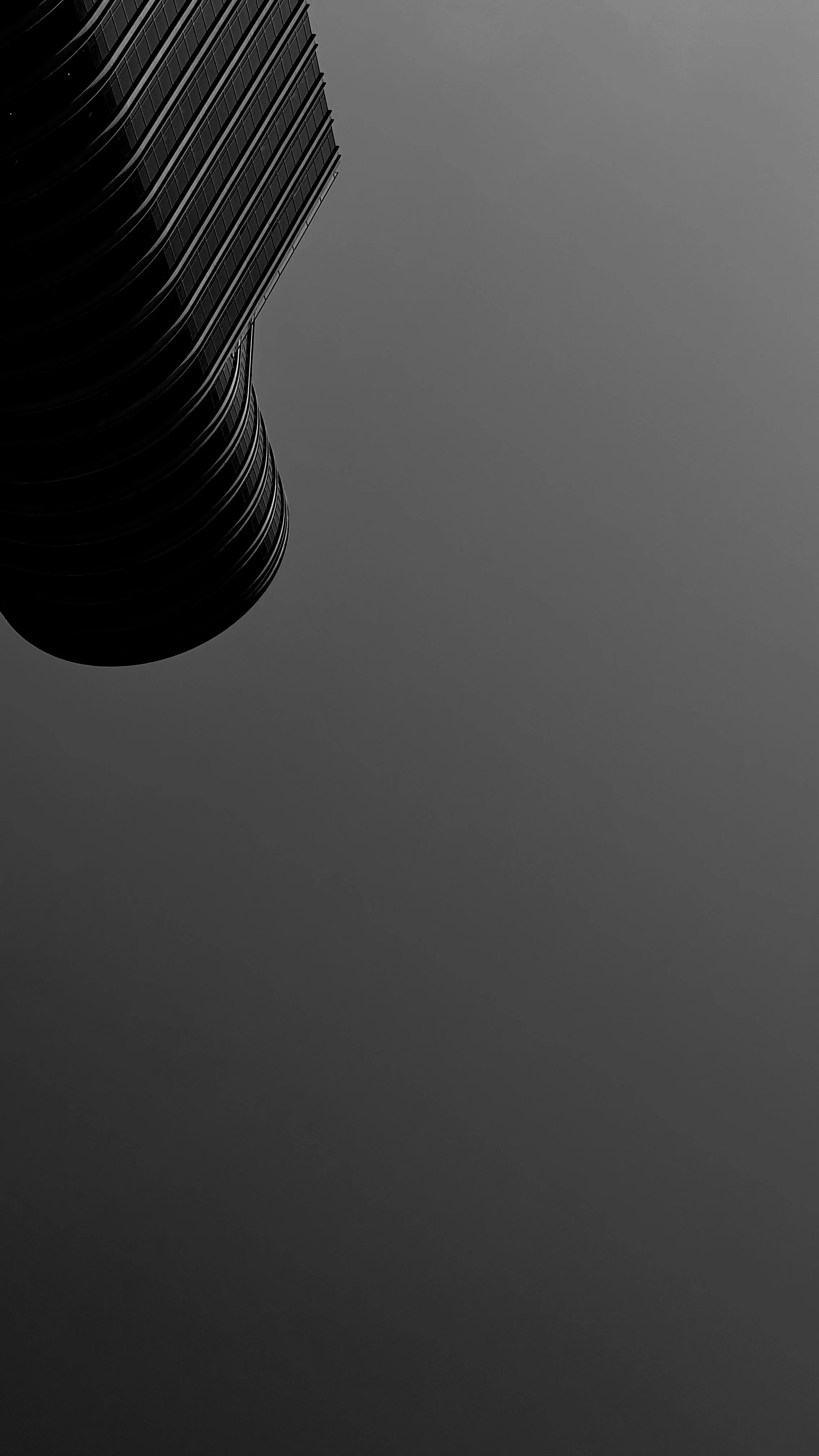 A tall, modern building with curved, reflective glass windows seen from below against a cloudy sky.