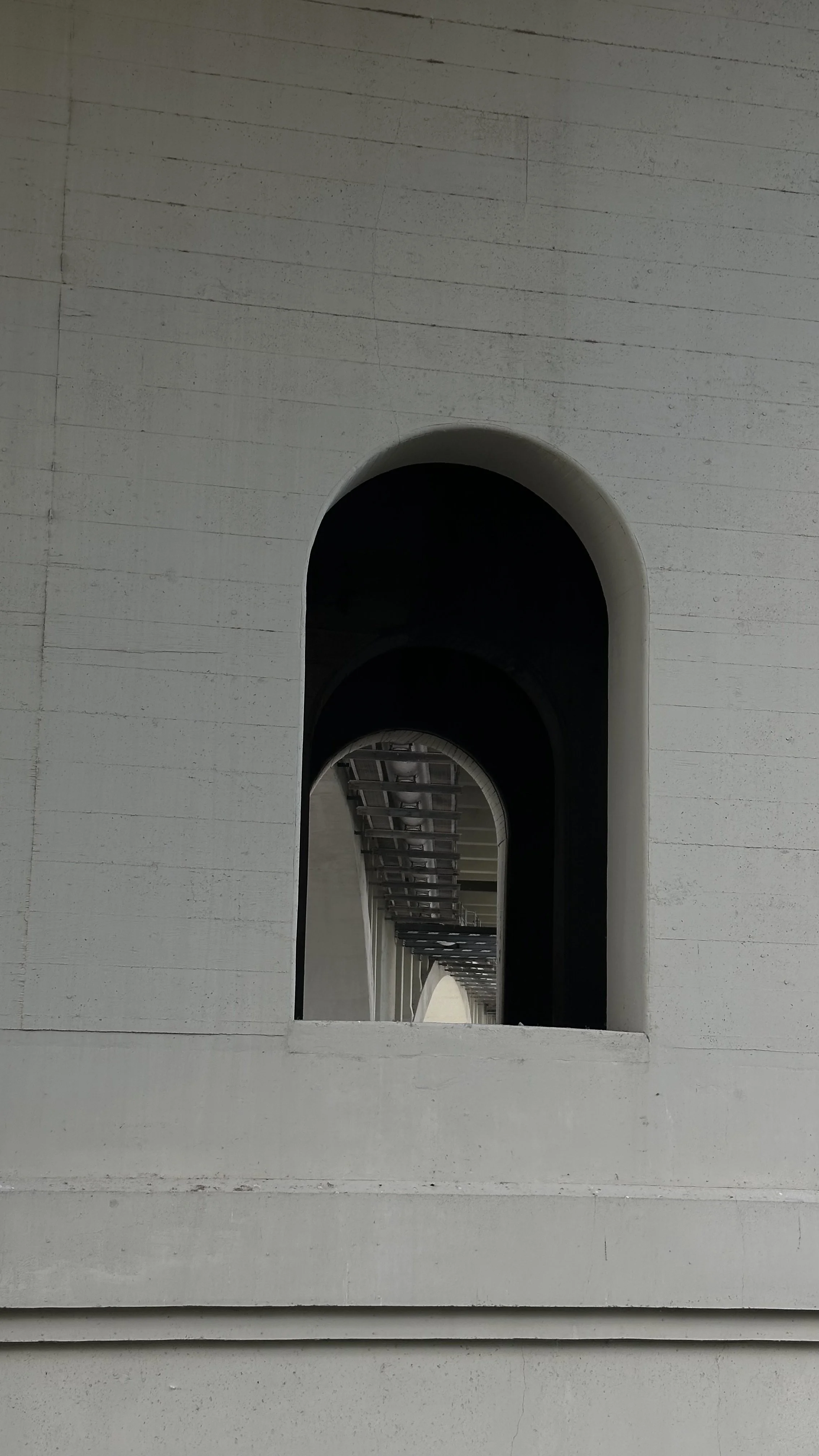 Concrete building with multiple arched openings, creating a visual tunnel effect.