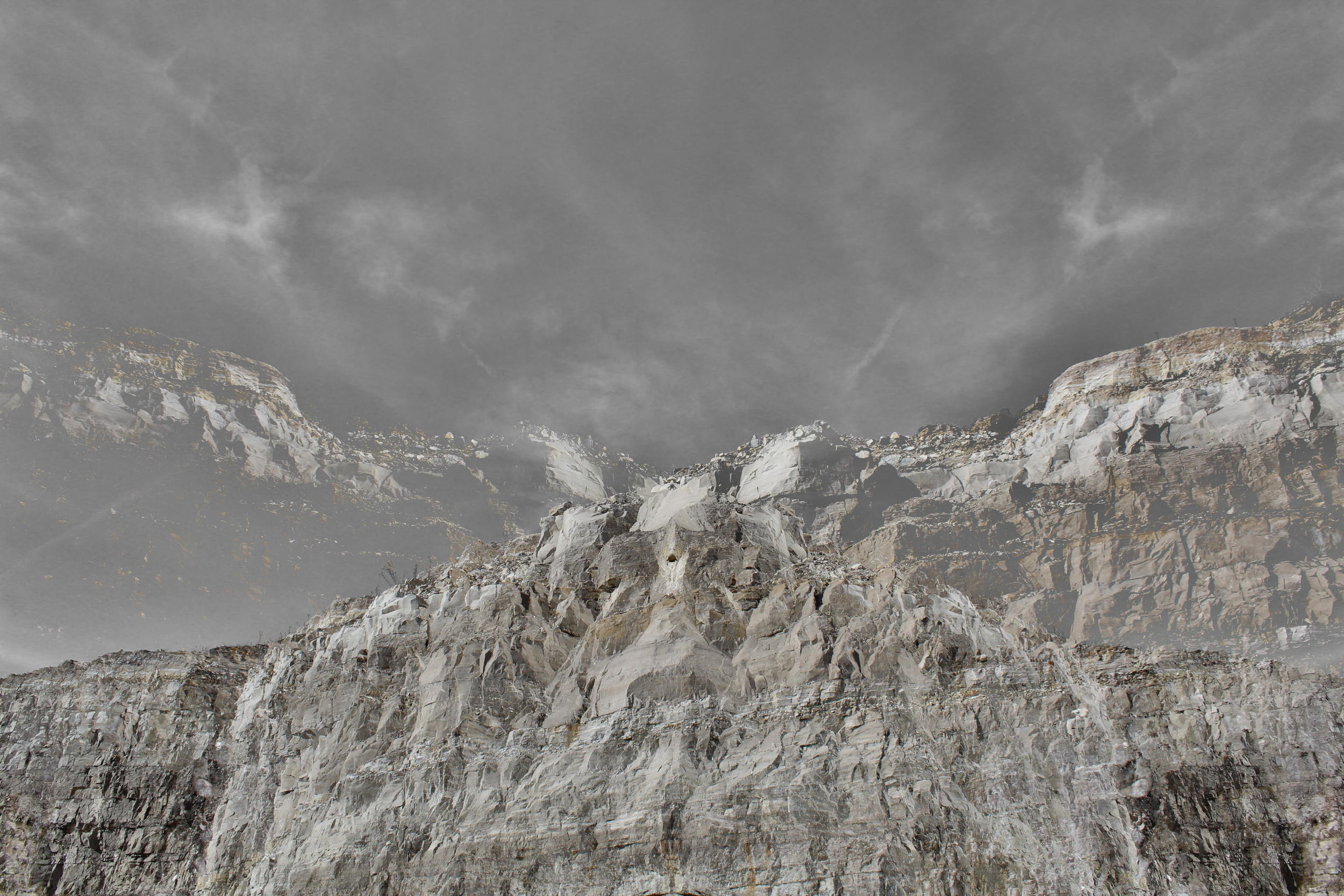 A rugged mountain landscape with steep rocky cliffs and a cloudy sky above.