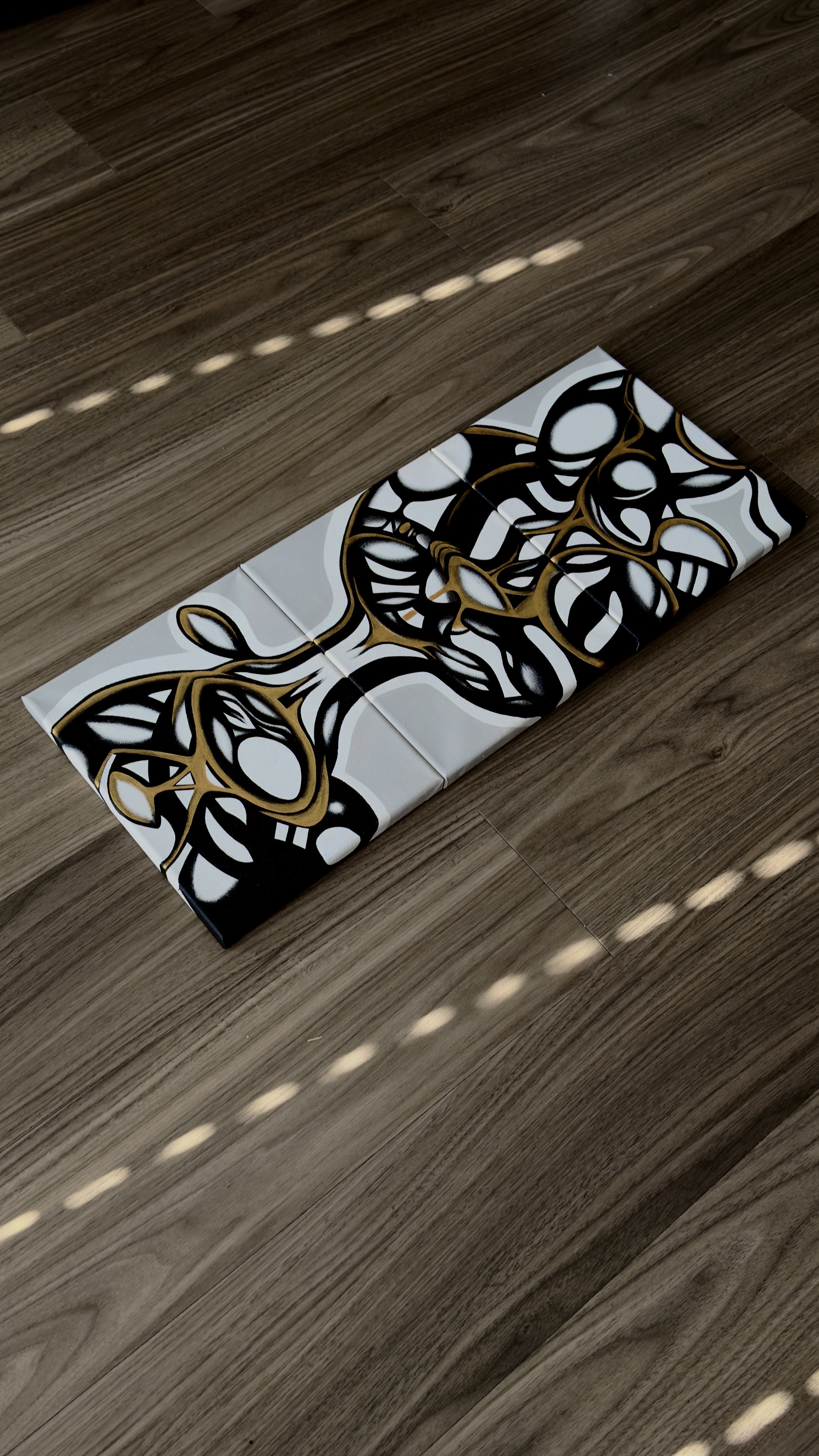 Decorative wall tiles with black, white, and gold abstract design on a wooden floor.