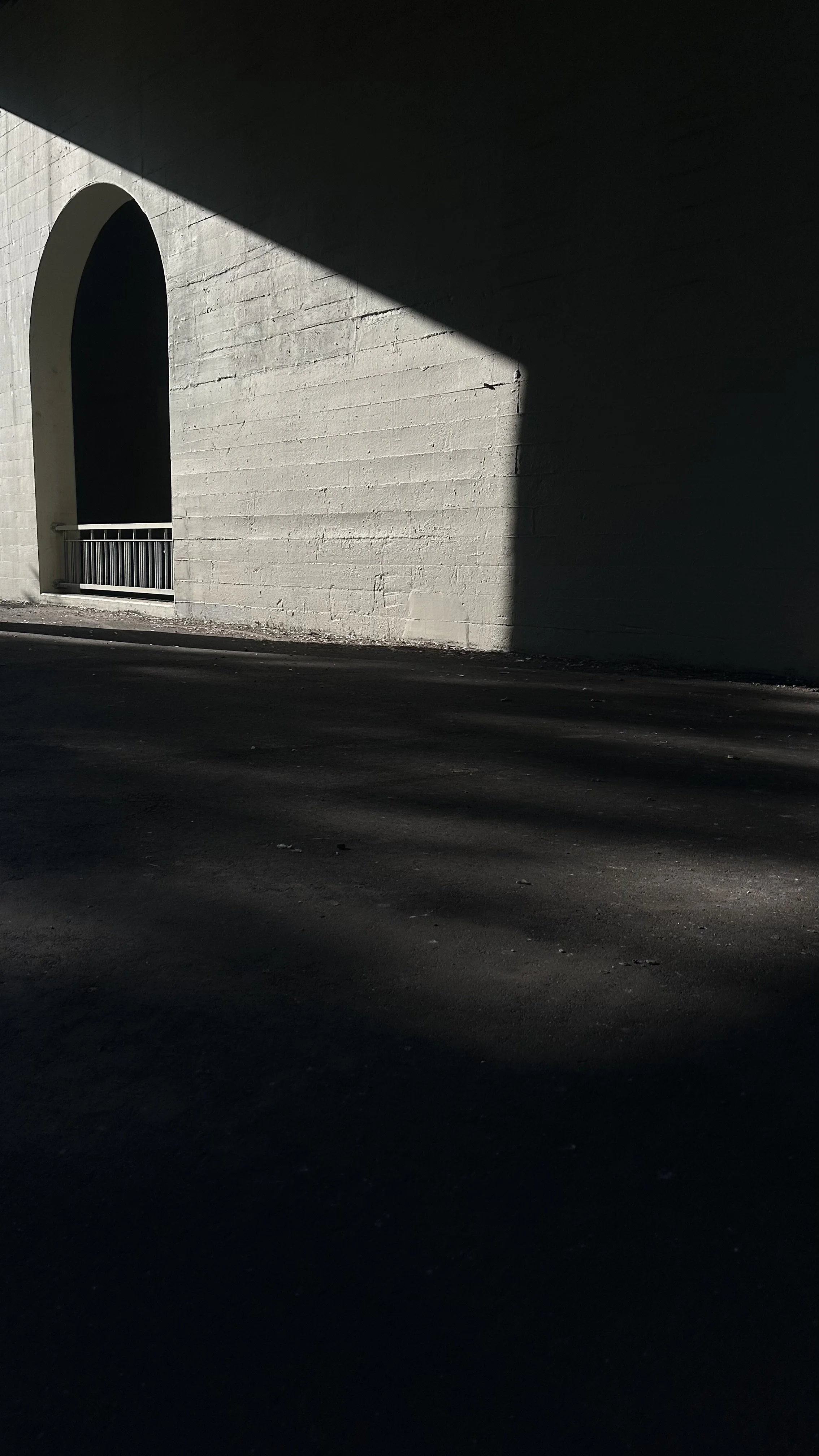 Shadows cast on a white brick wall and dark asphalt road underneath an overpass or bridge.