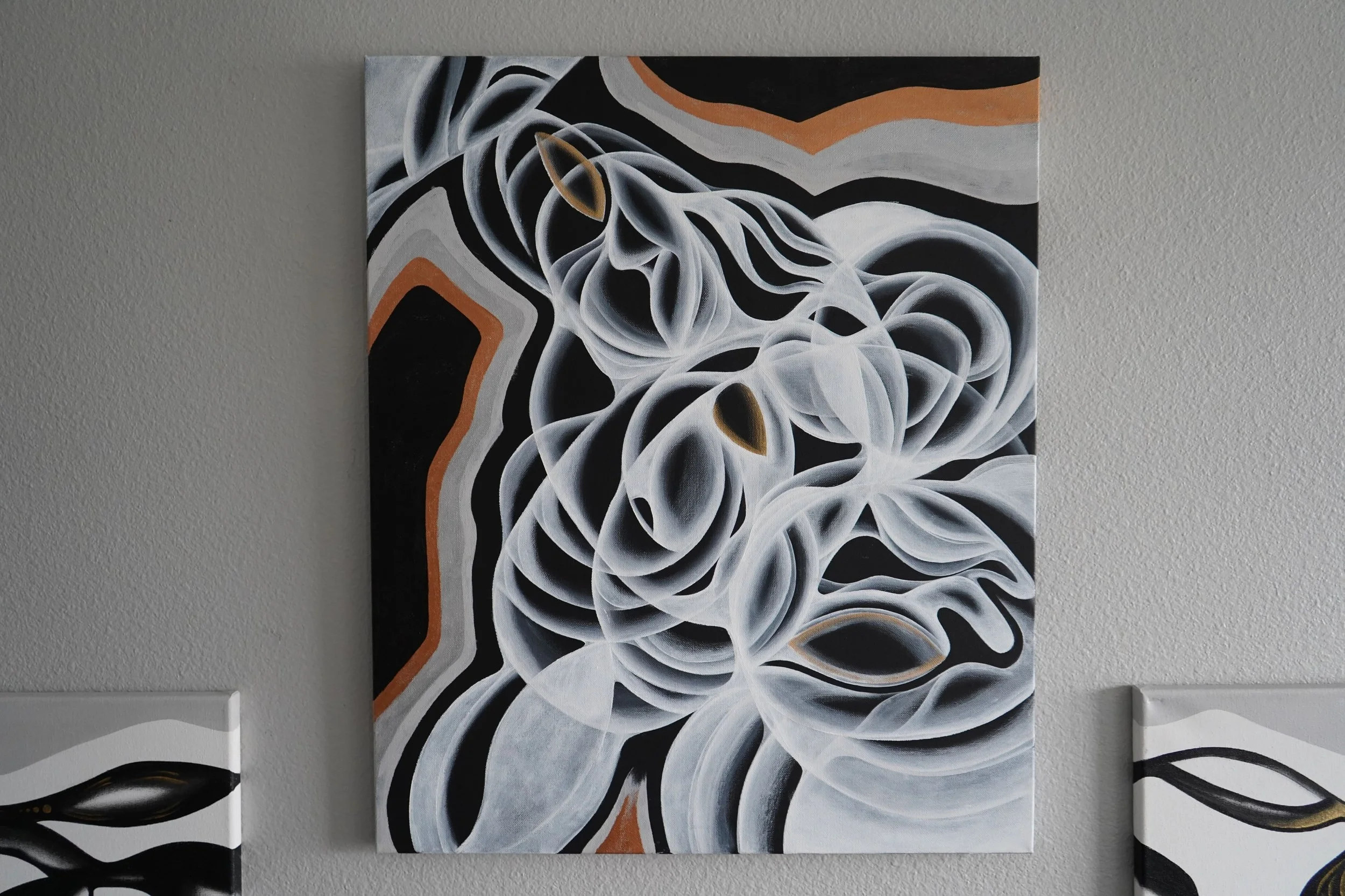 Abstract black, white, gray, and orange painting of swirling shapes and flowing lines on a wall.