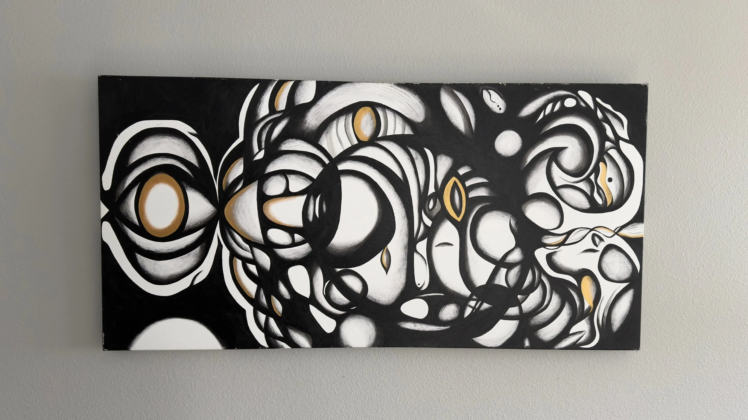 Abstract black and white painting with gold accents on a gray wall.