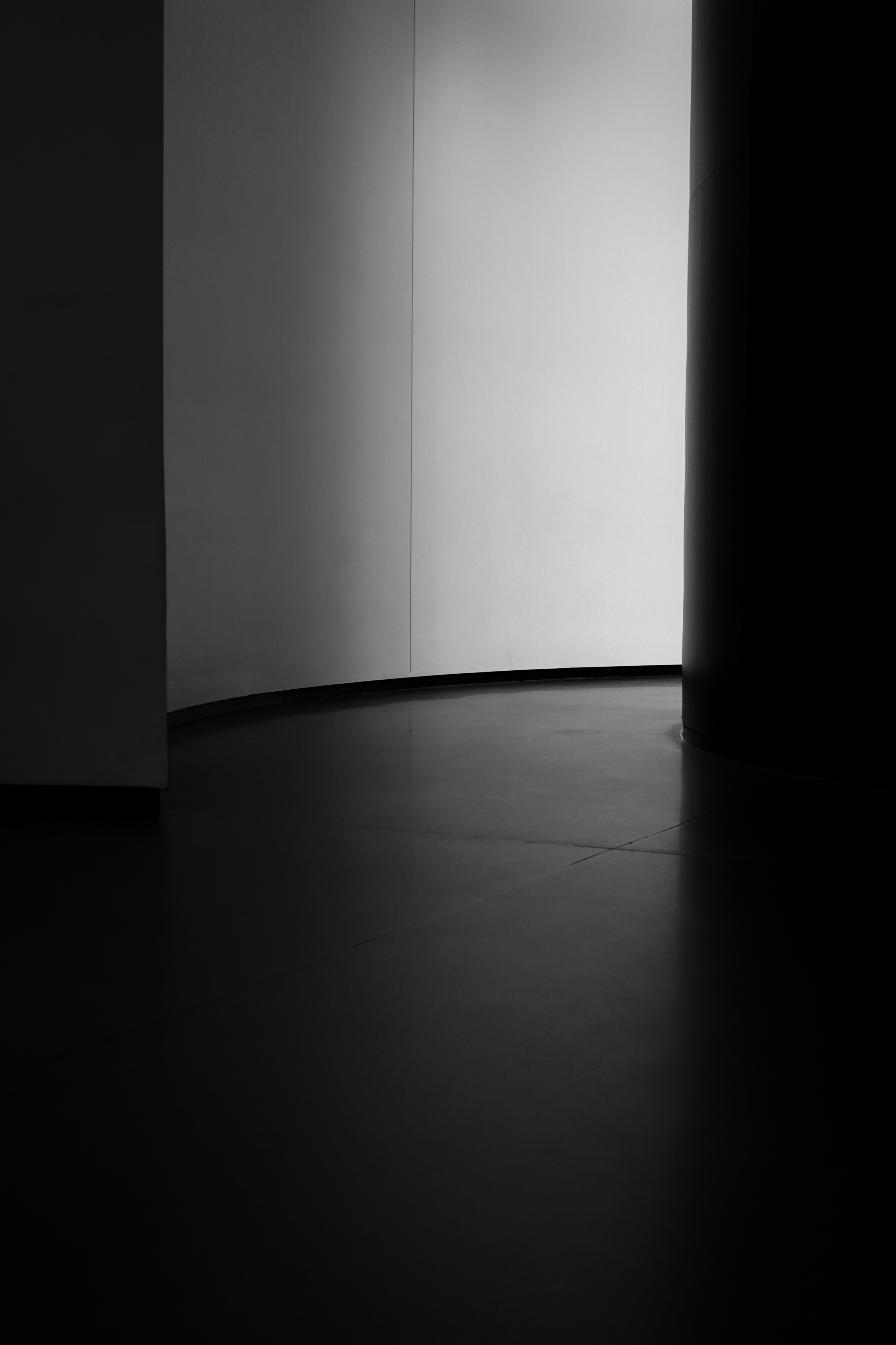 A grayscale image of a curved, brightly lit wall with surrounding darkness.