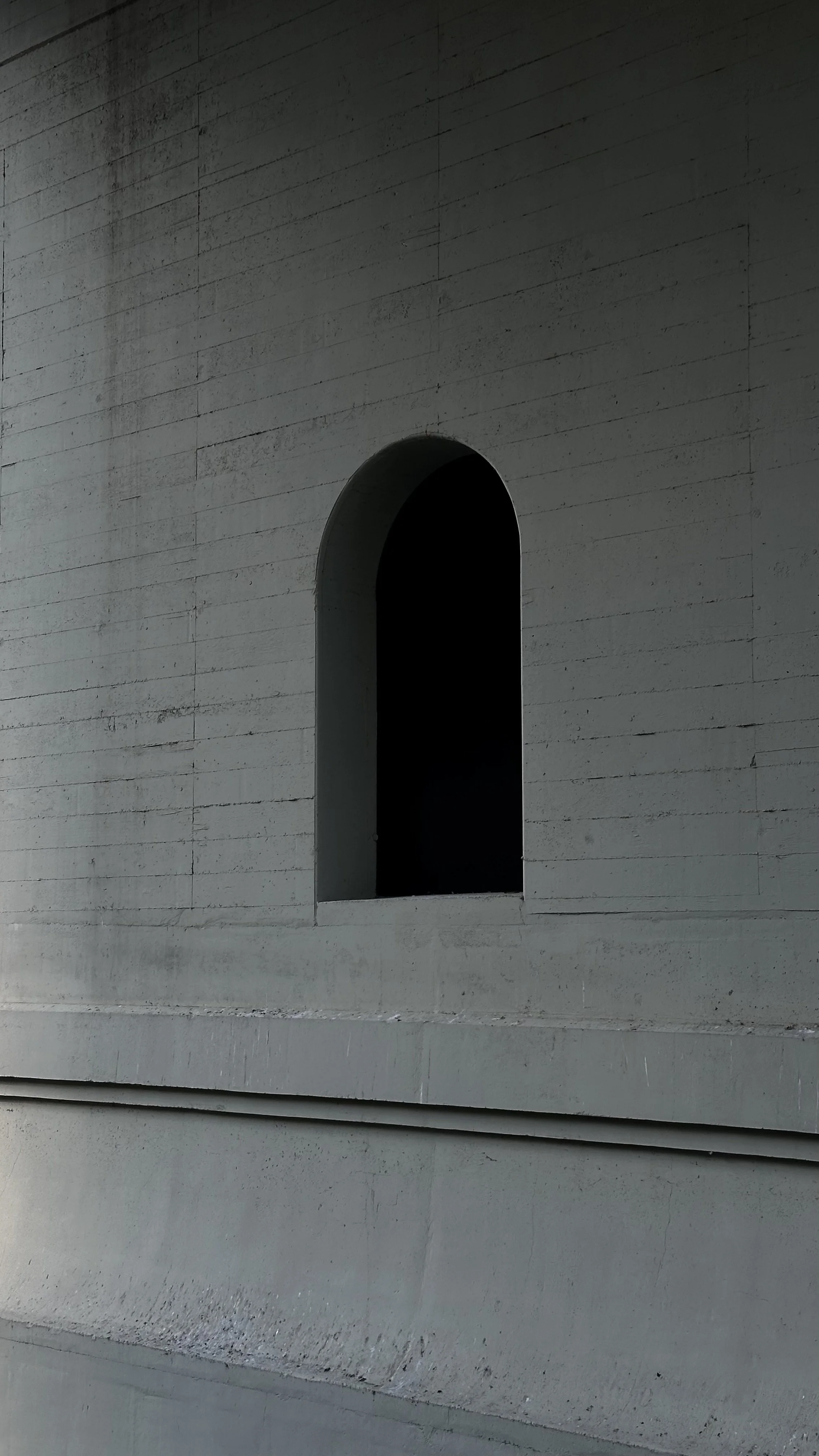 A large, gray concrete wall with a black arched window opening.