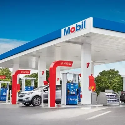 A Mobil gas station with multiple fuel pumps and vehicles fueling up, under a blue and white canopy with the Mobil logo.