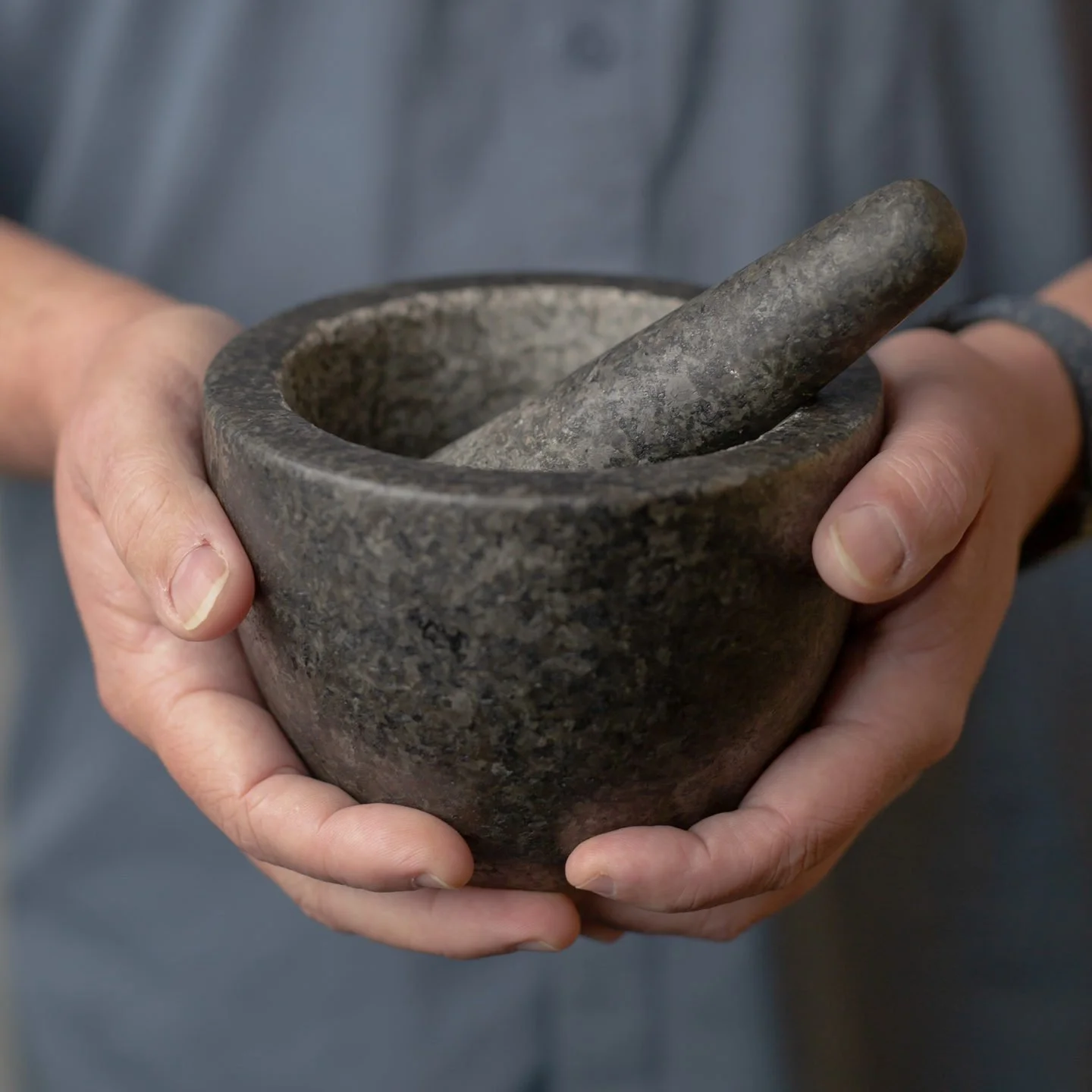 A person holding a stone mortar and pestle, used for grinding or pounding ingredients.