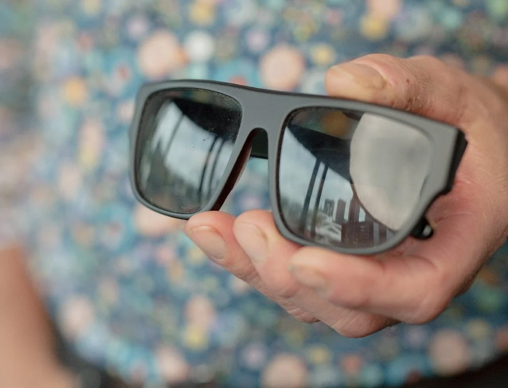 A hand holding a pair of 3D glasses with the city skyline reflected in the lenses.
