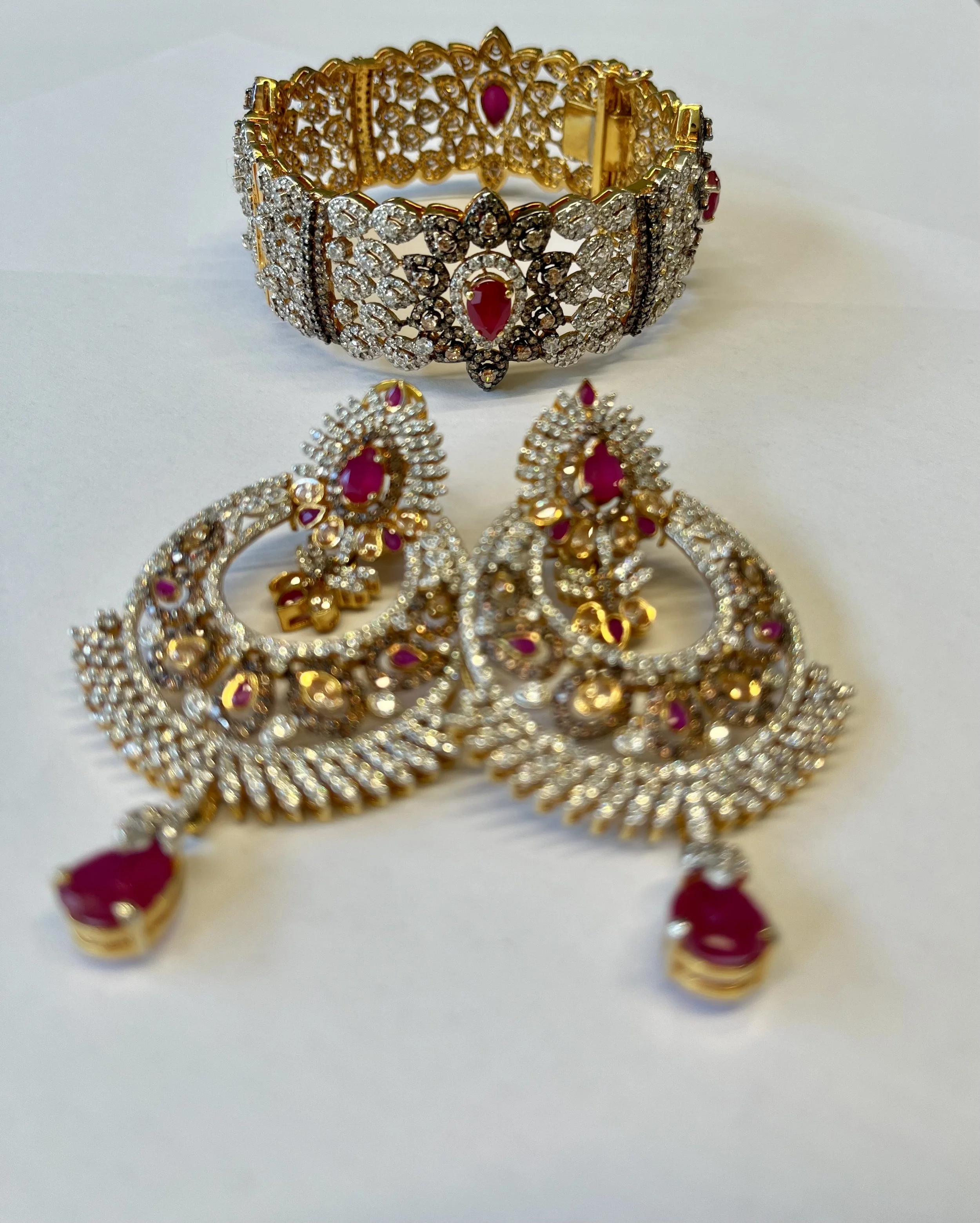 Gold and silver jewelry set including a pair of earrings and a bracelet with red and clear stones on a white background.