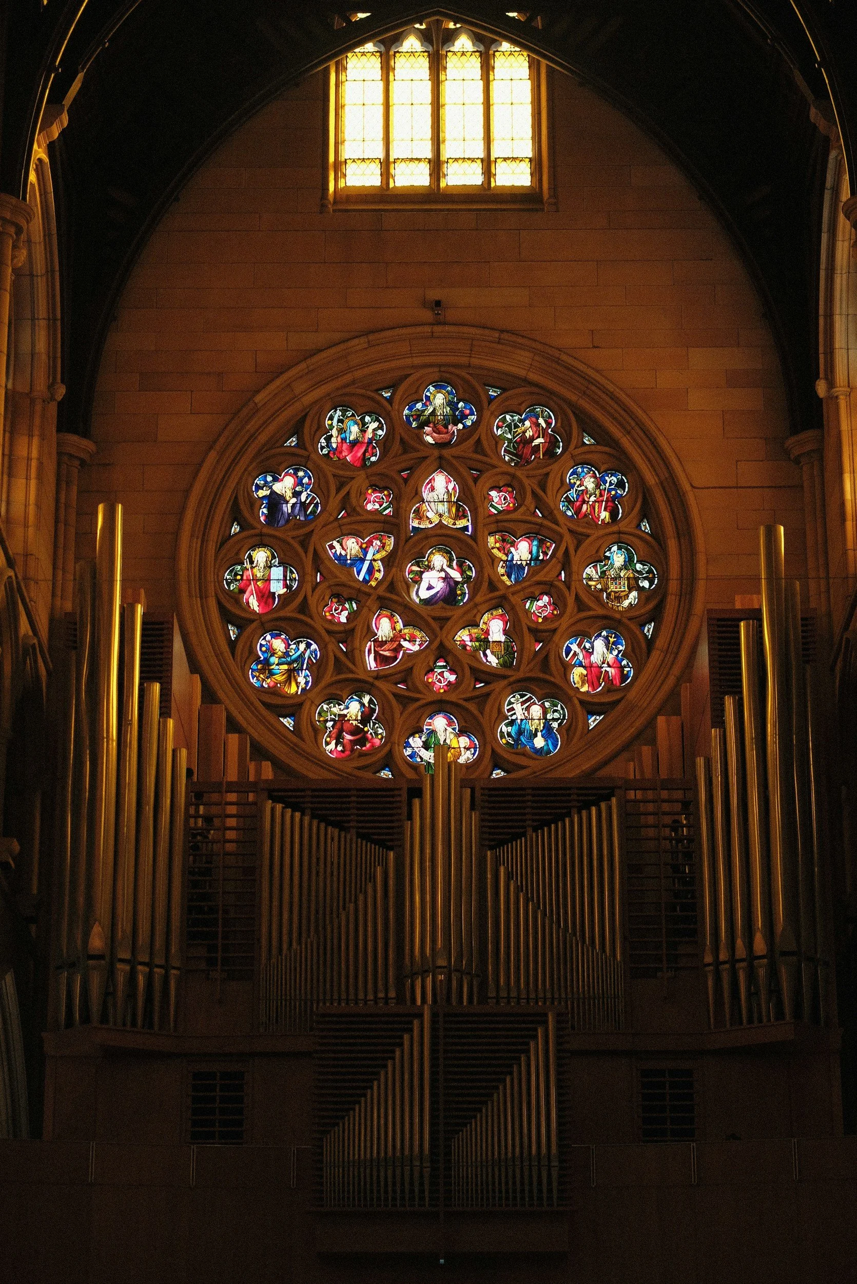 Interior of a church with a large stained glass window featuring religious figures and a pipe organ beneath it.