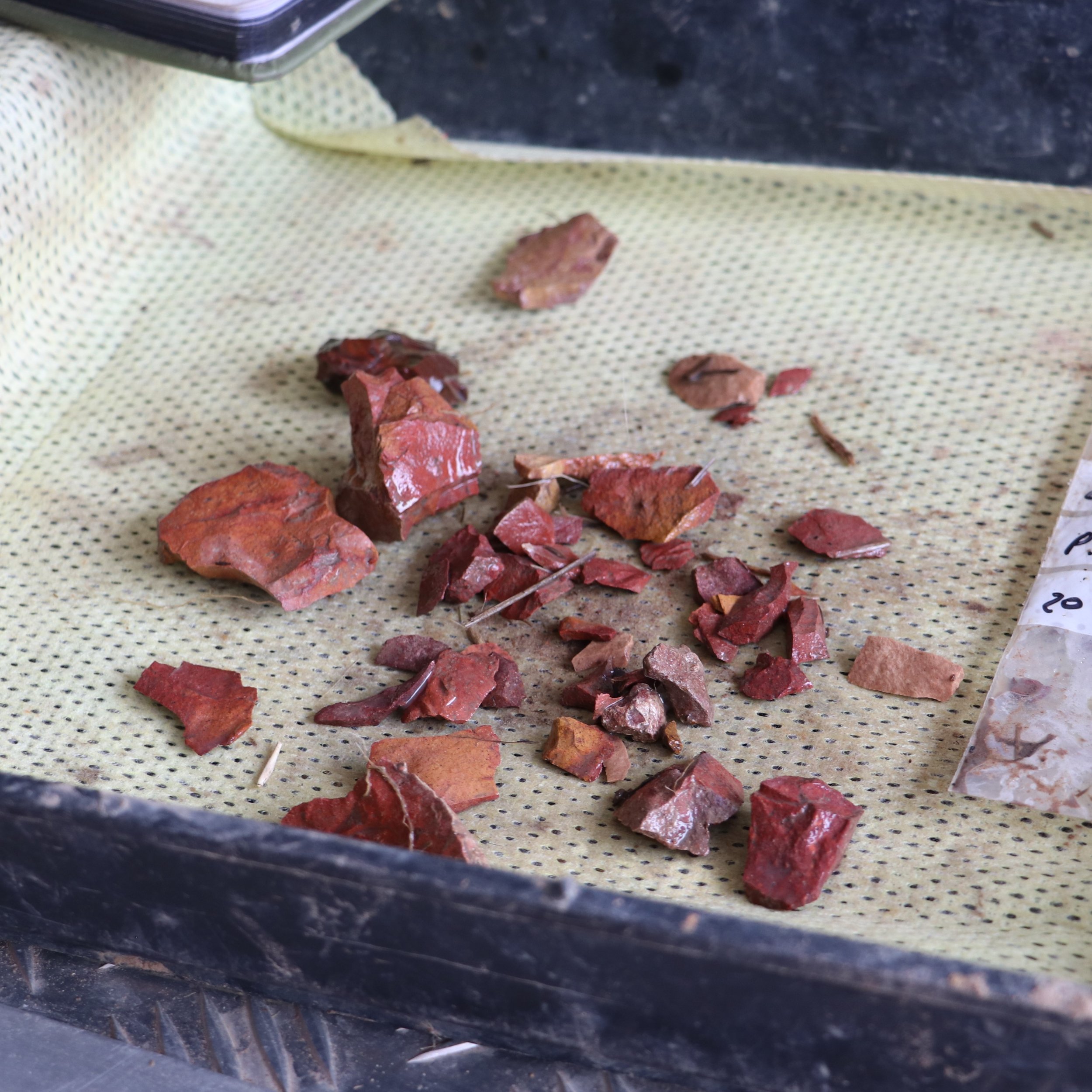 Irregular red and brown rocks on yellow perforated paper, with a black object at the top edge of the image.