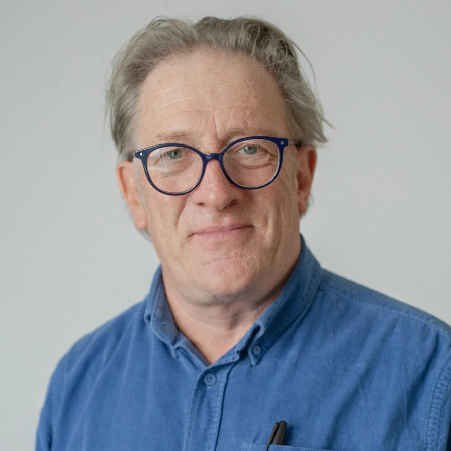 A middle-aged man with gray hair and glasses wearing a blue button-up shirt, looking slightly to the side against a plain background.