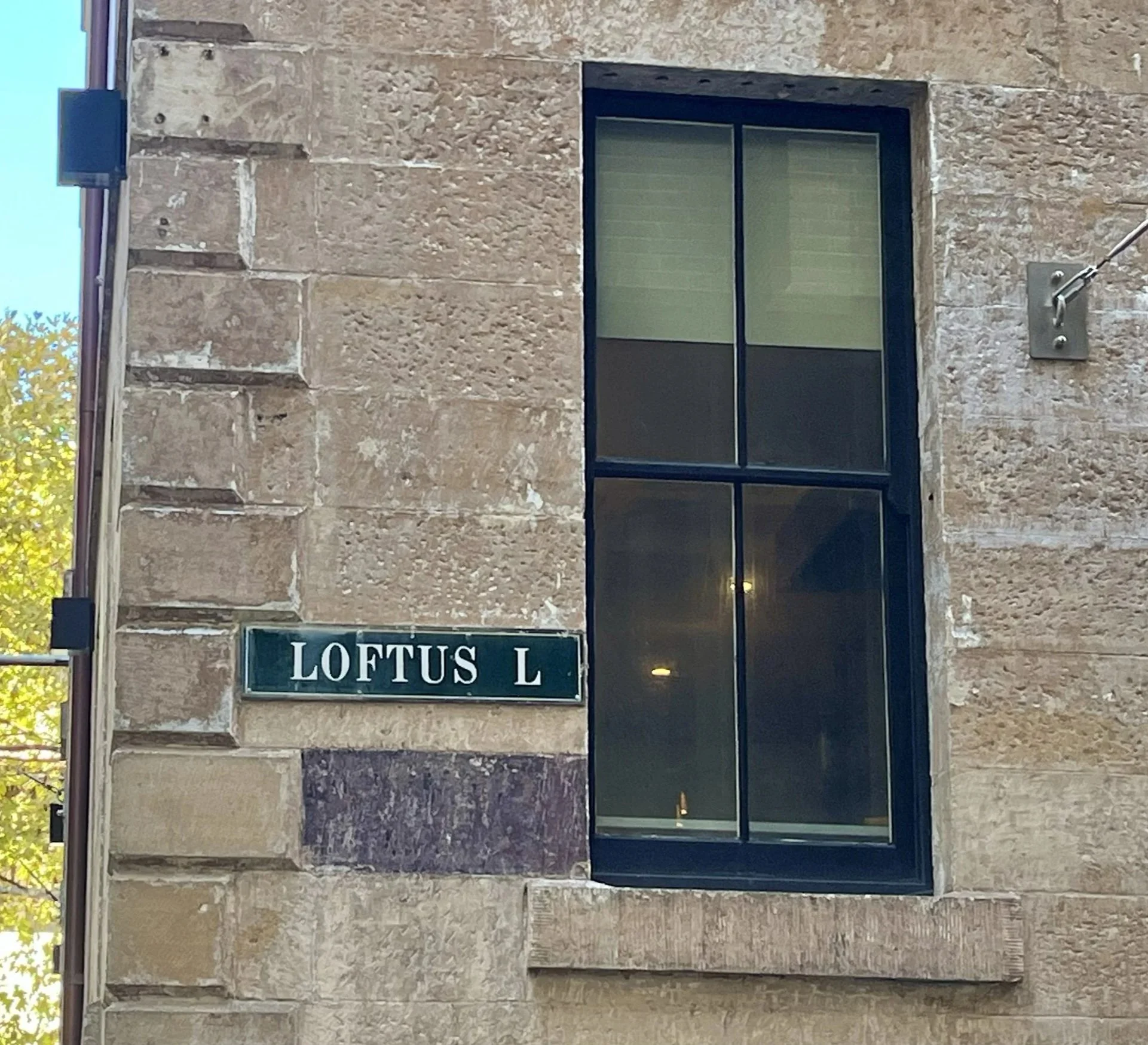 Close-up of a brick building with a large black window and a street sign that reads 'LOFTUS L'.