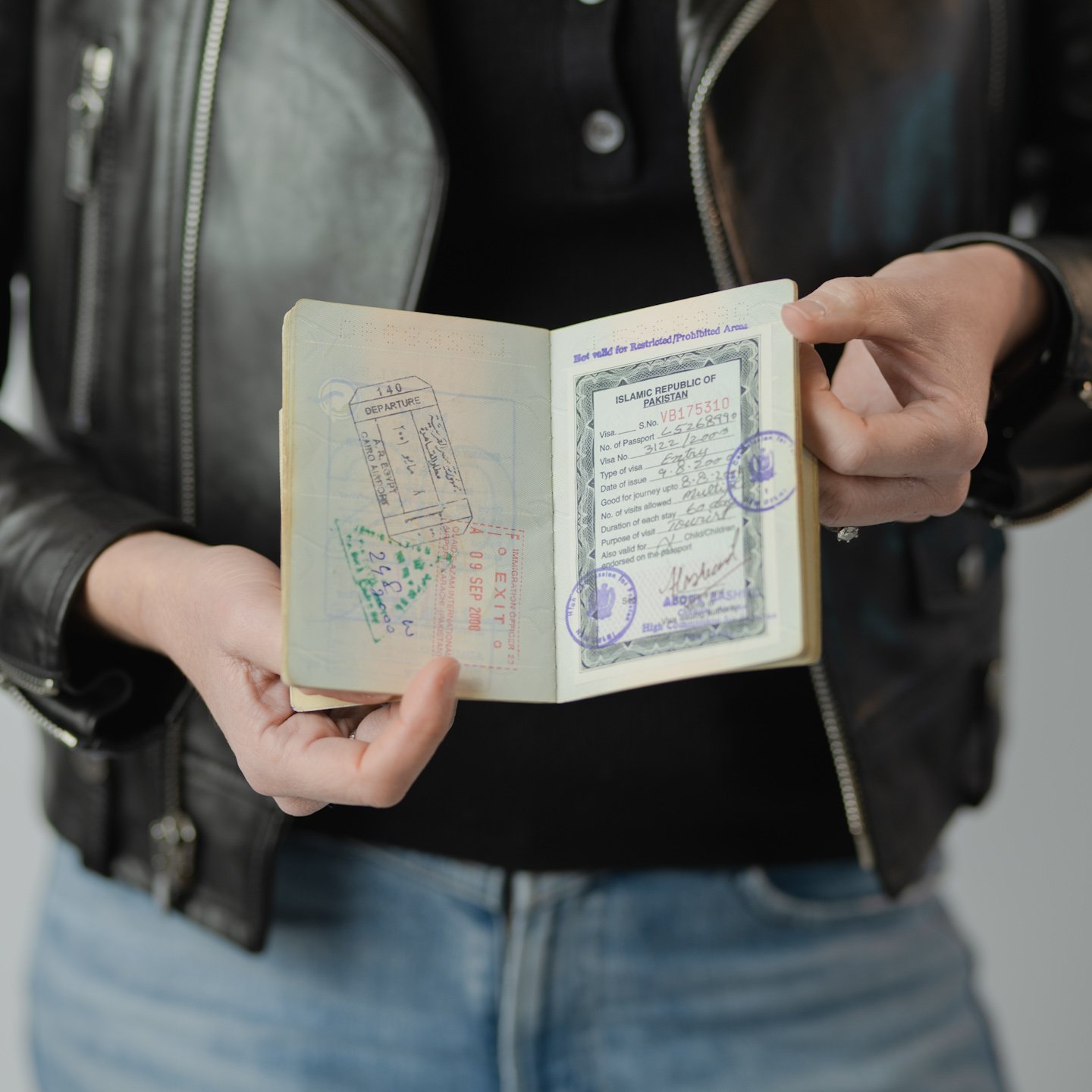 Person holding a passport open to visa pages with stamps and travel details.