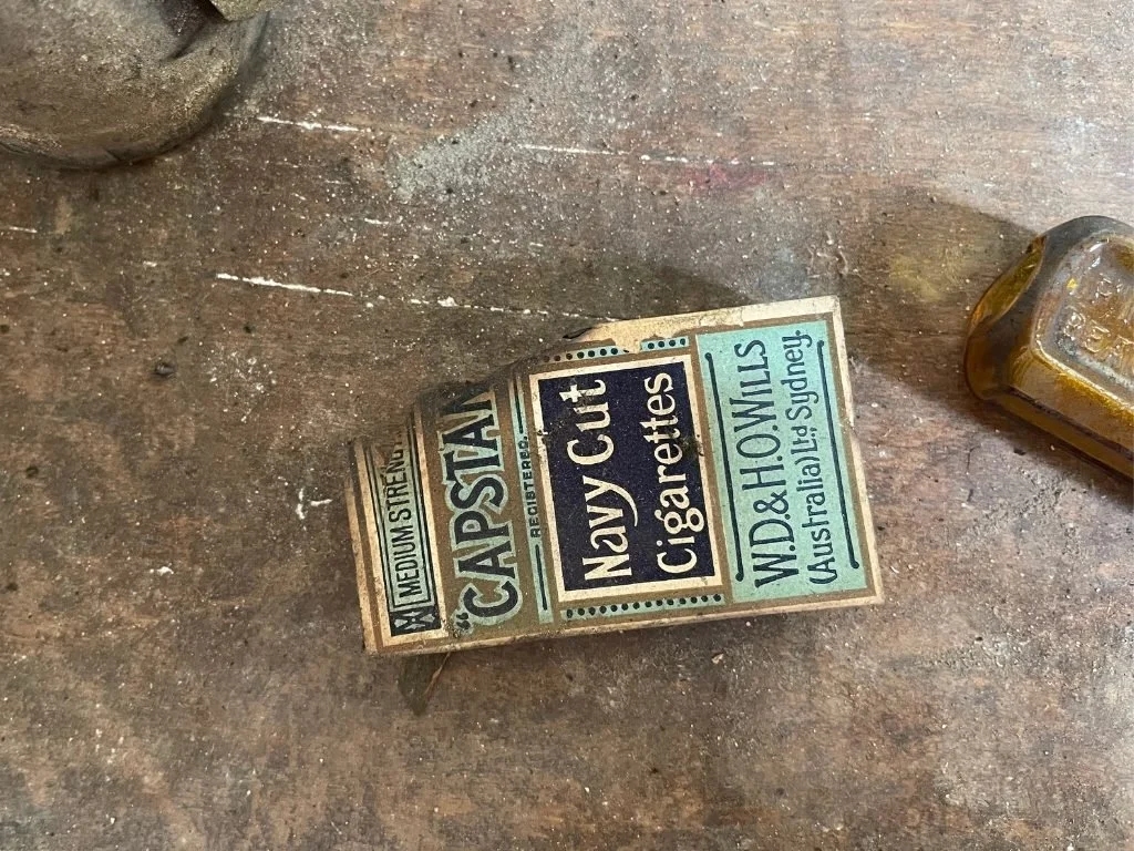A vintage box of navy cut cigarette filters on a wooden surface, with some white powder and a glass container nearby.