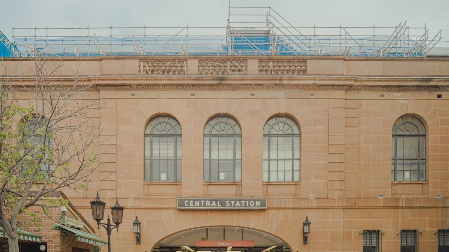 Facade of a building with a sign that reads 'Central Station' and tall arched windows, with construction scaffolding on the roof.