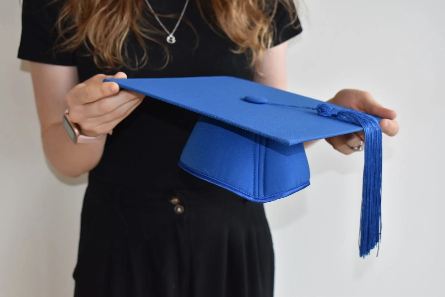 Person holding a blue graduation cap with a tassel, celebrating graduation.