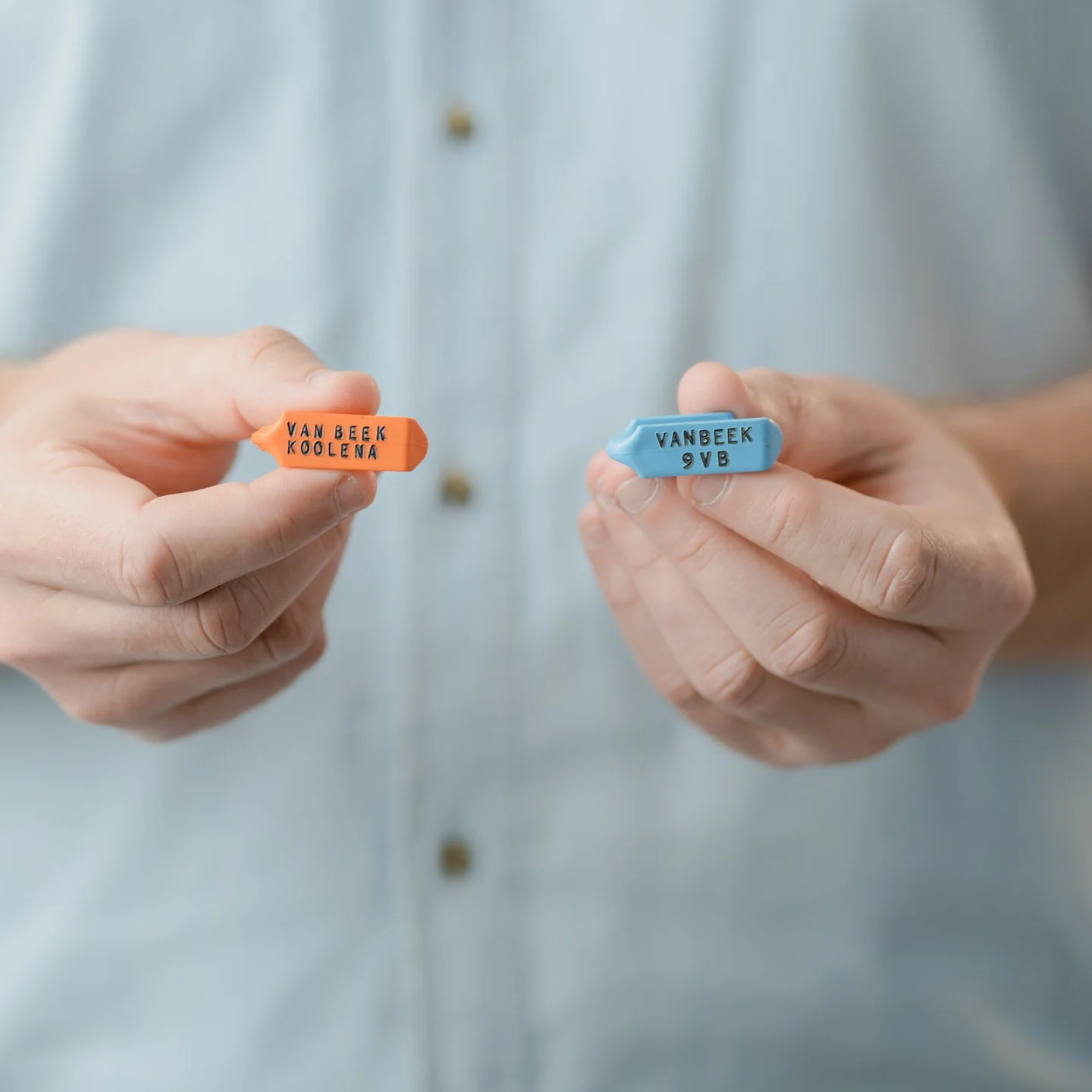 Hands holding two colored dental impression trays labeled with the brand name VanBeek, one orange and one blue.
