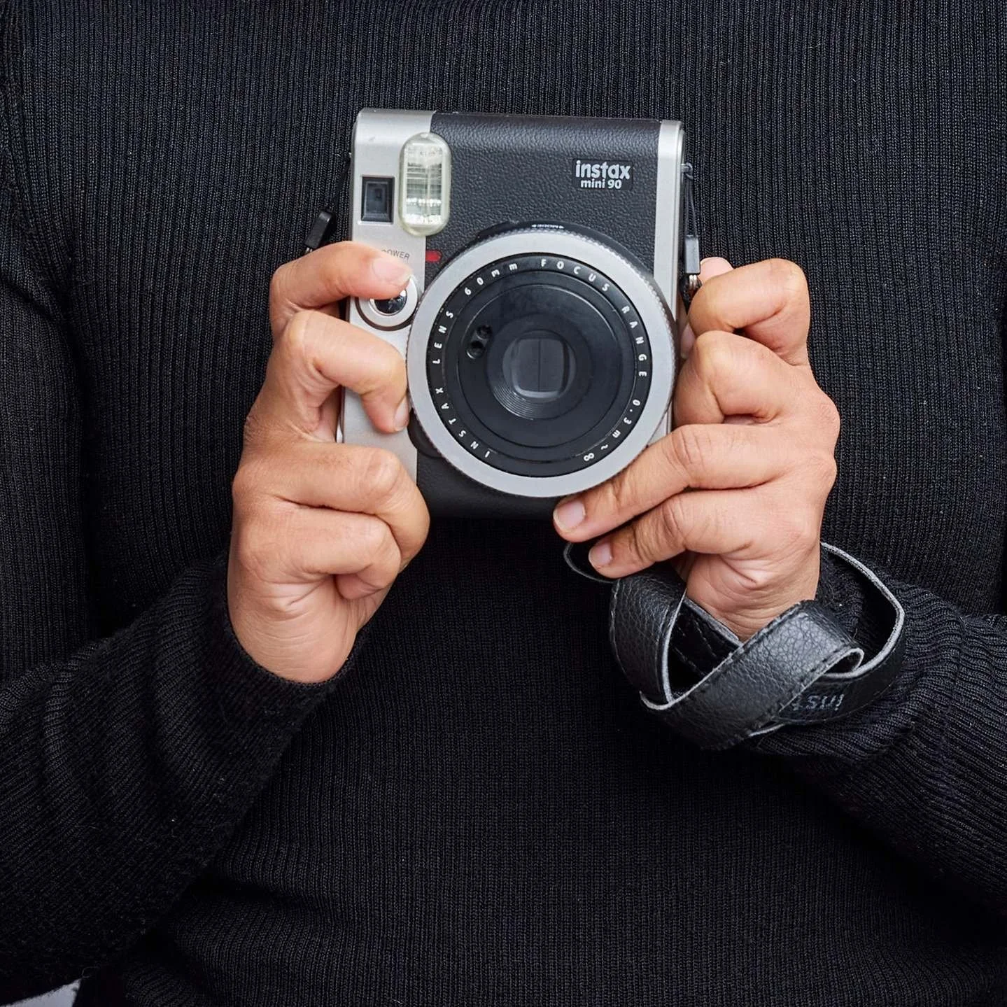 Person holding a vintage film camera, wearing a black sweater with a leather strap.
