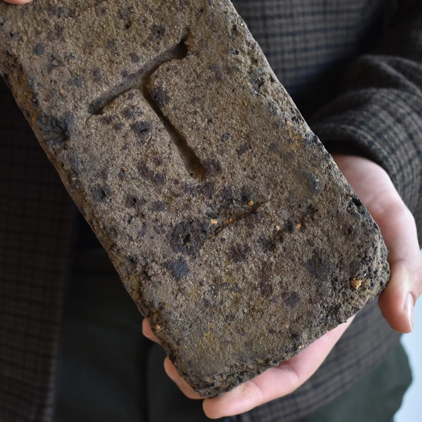 A person holding a rectangular brick with a rough surface and the letter 'F' engraved on it.
