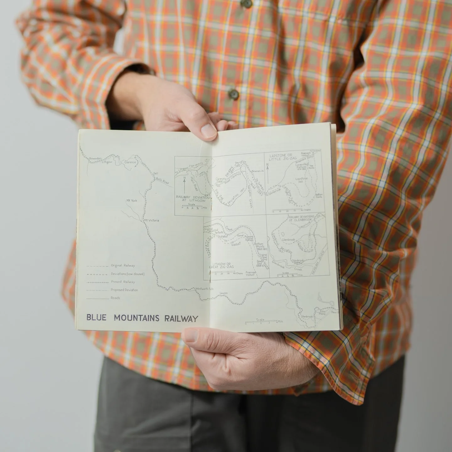 A person in an orange plaid shirt holding a map of the Blue Mountains Railway, showing railway routes and deviations in detailed sections.