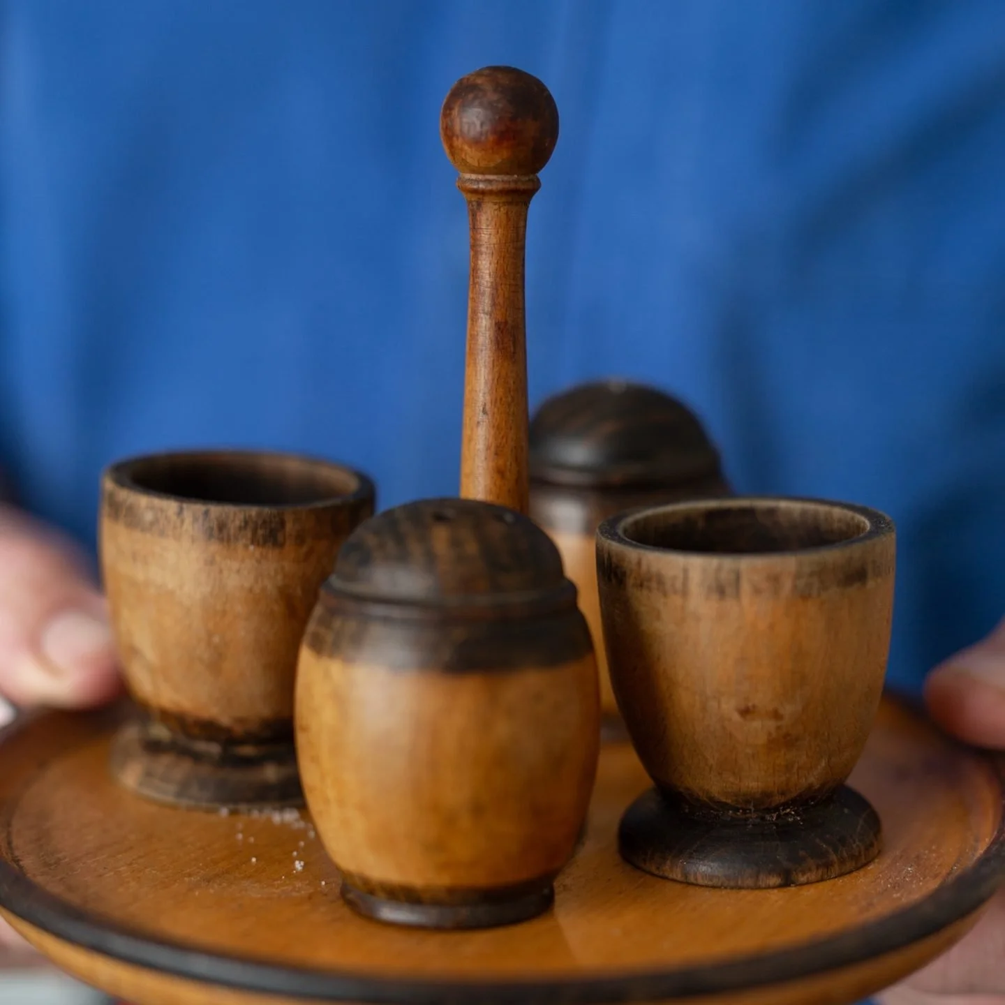 Close-up of a wooden chess set with a pawn in the center and other pieces around, held by hands against a blue background.