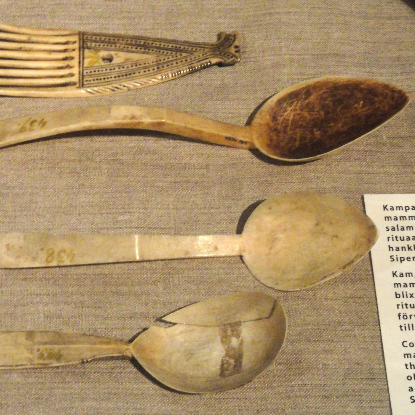Three ancient carved spoons with different shapes and designs displayed on a textured surface.
