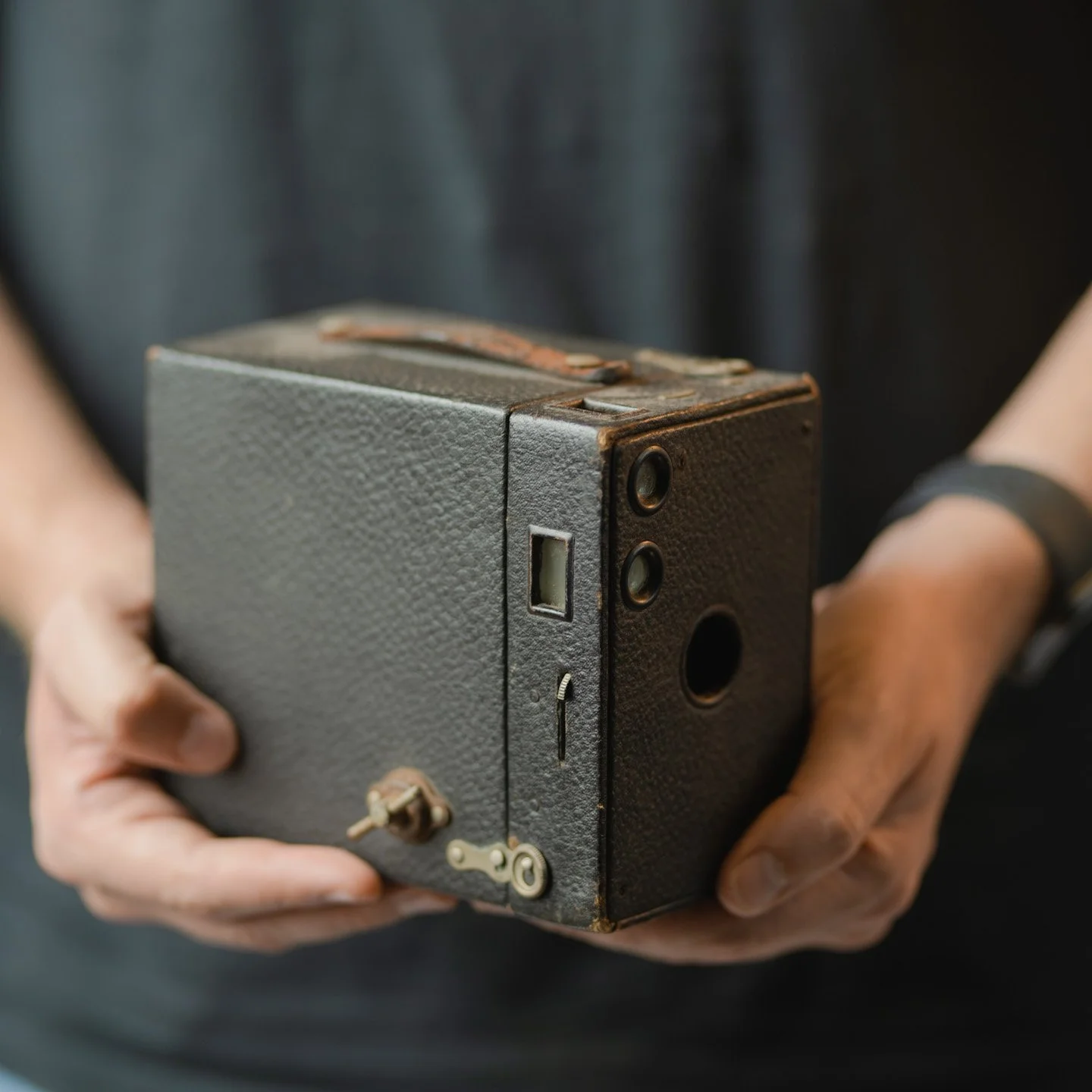 Person holding a vintage box camera with a textured gray surface.