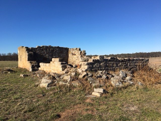 Ruined stone structure in an open field under a clear blue sky.