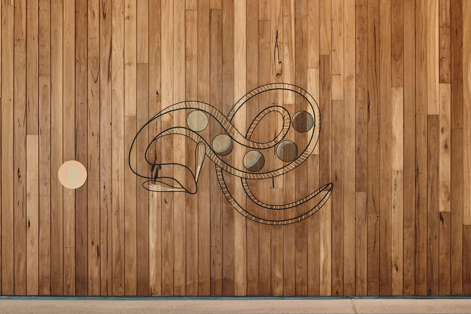 Modern wall art sculpture of a stylized whale and fish, made with metal outlines and circular elements, mounted on a wooden panel wall.